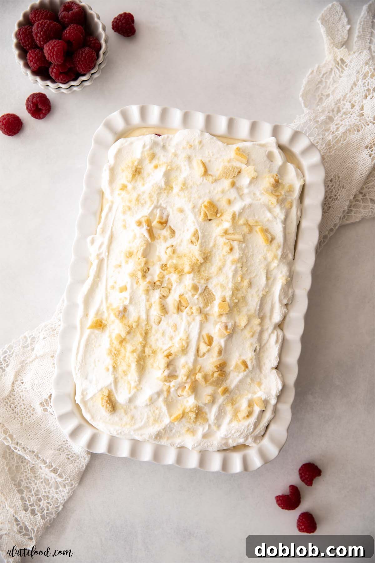 Chilled White Chocolate Raspberry Pudding with whipped cream and crushed butter cookies in a white baking dish.