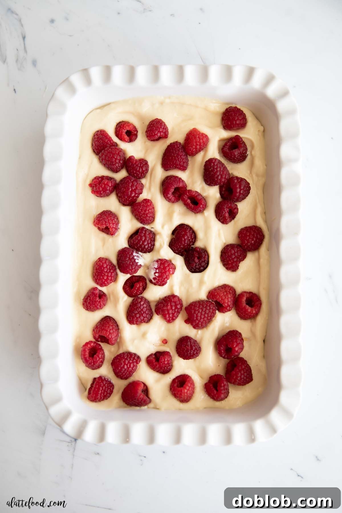 White baking dish filled with layers of raspberry pudding and fresh raspberries, ready to be served.