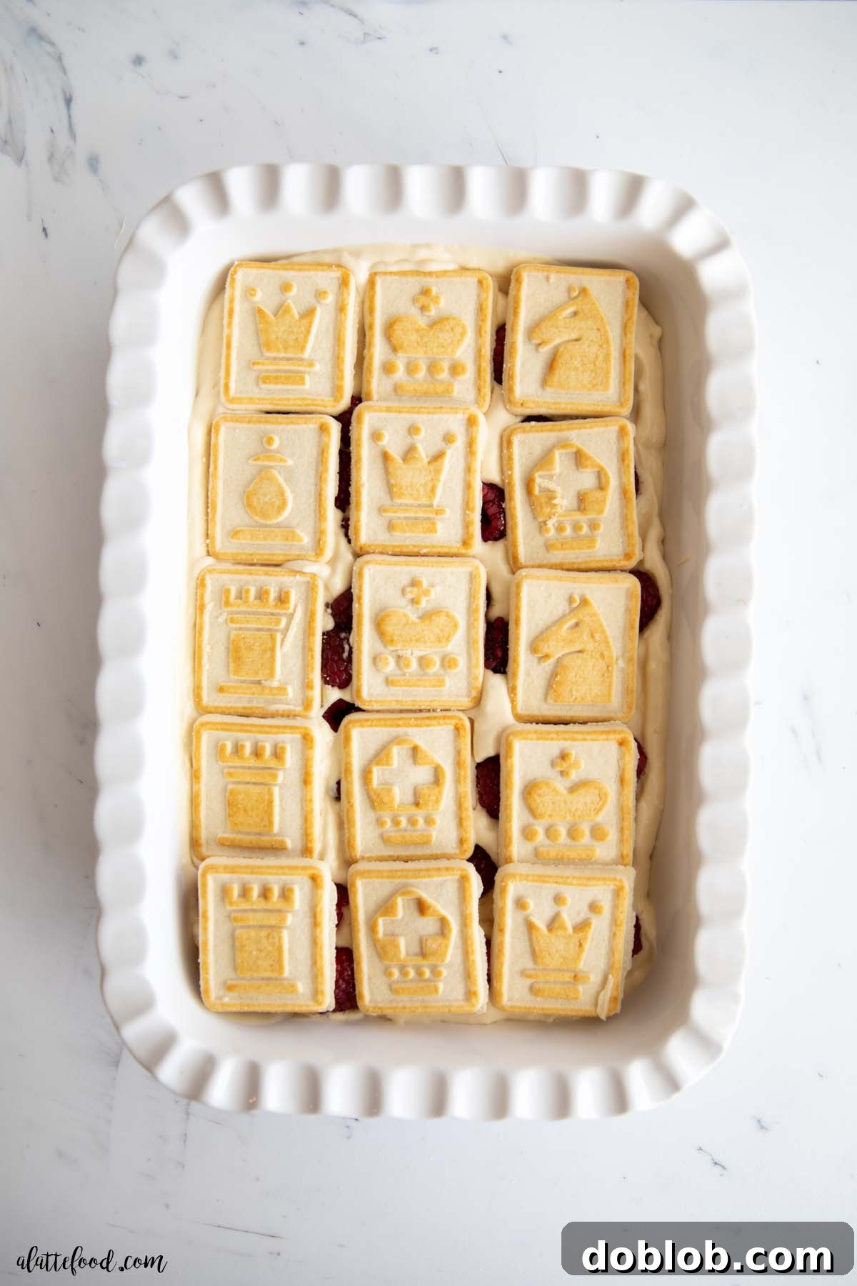 White baking dish with white chocolate pudding, fresh raspberries, and chess cookies layered inside.