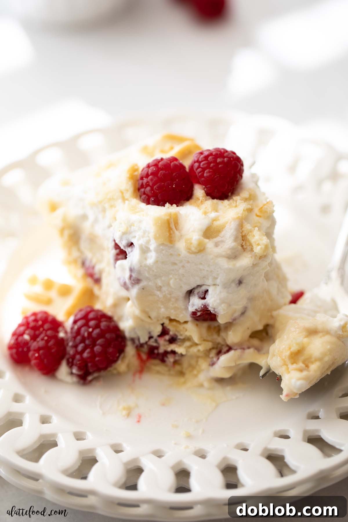 Layered Raspberry Pudding dessert with a fork on a white plate, ready to be enjoyed.