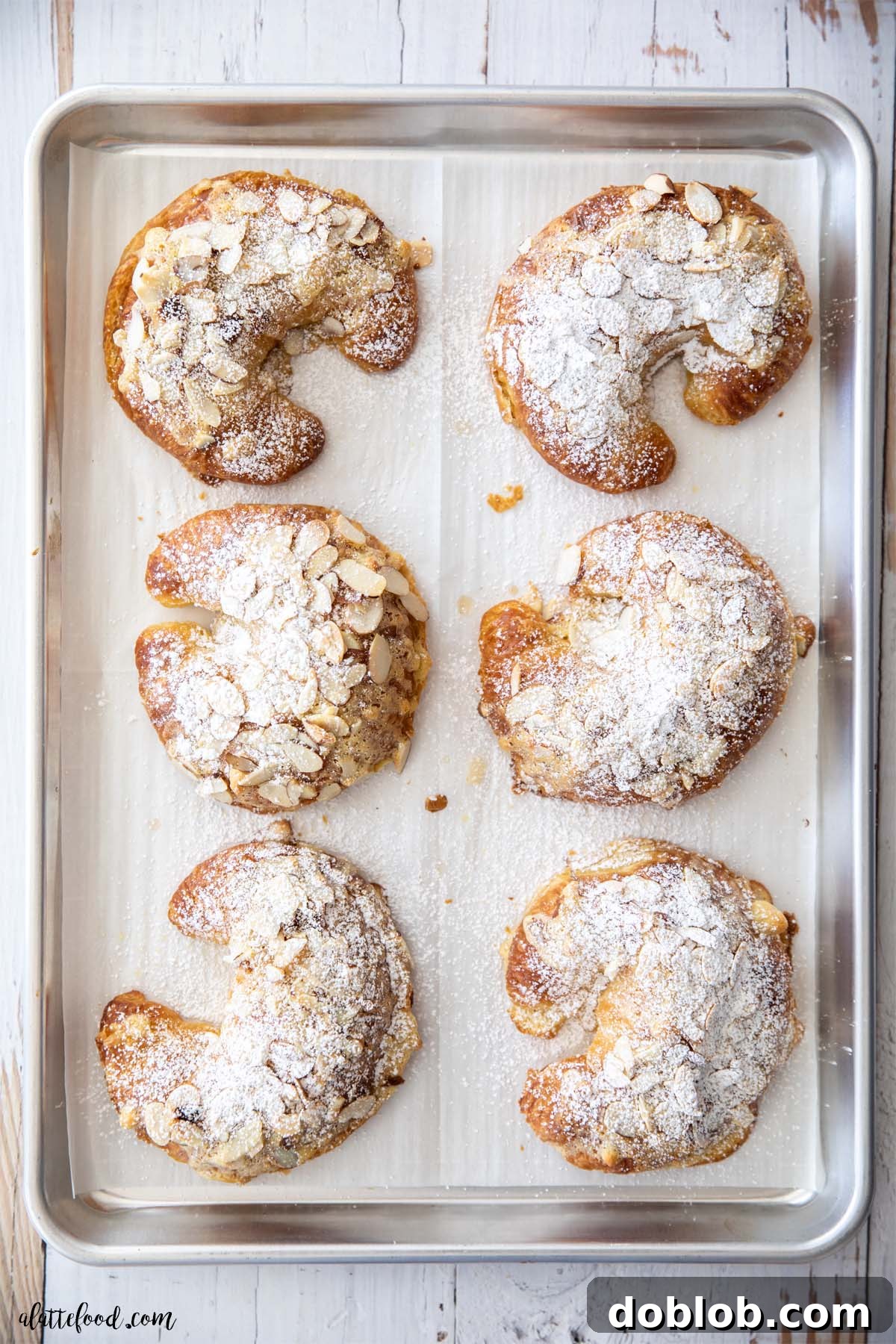 Almond Croissants are flaky and buttery and filled with almond frangipane made with almond paste. baked almond croissants with powdered sugar on a metal baking tray. Golden brown and perfectly dusted.