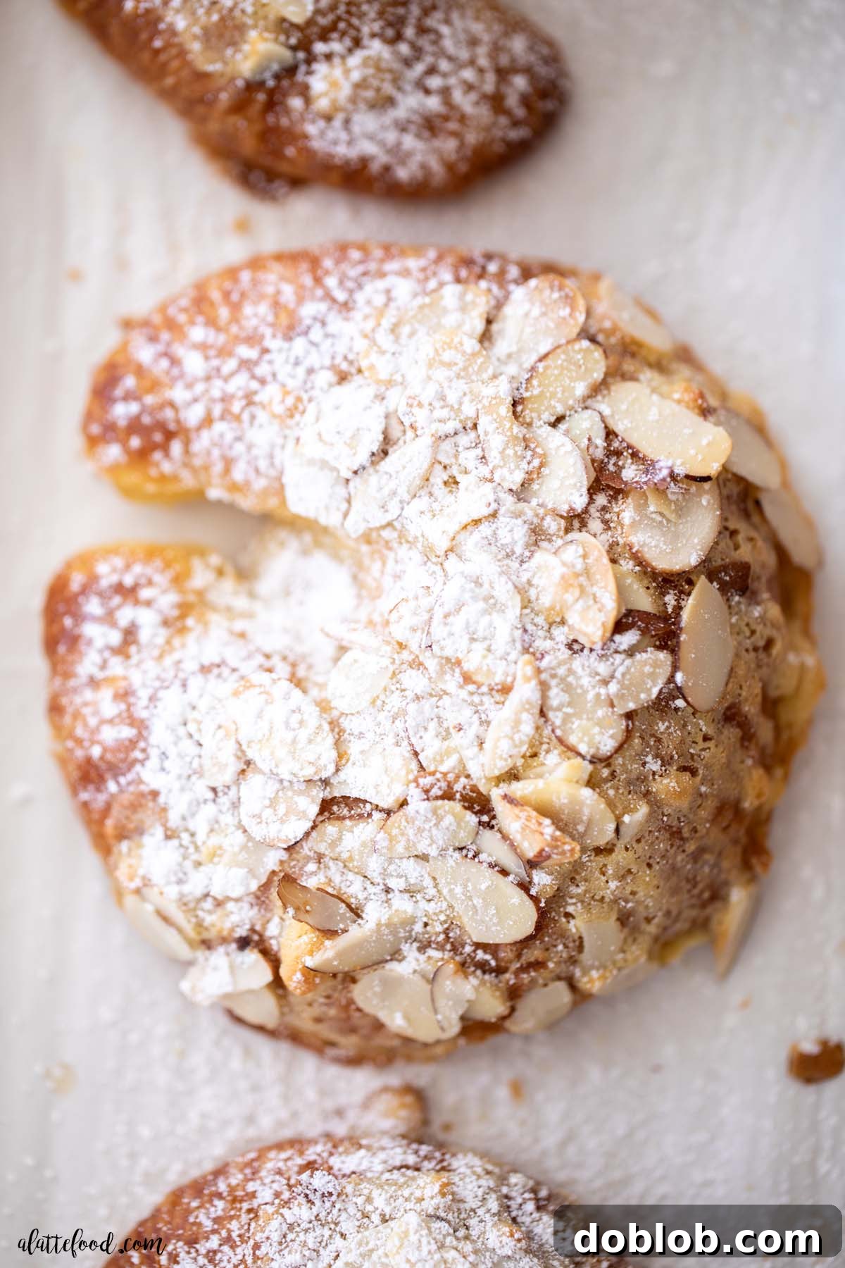 Homemade Almond Croissants are flaky, day old croissants that are filled with a sweet almond frangipane cream (made with almond paste) and topped with a simple syrup. Powdered sugar covered almond cream filled croissants. Delicious and sweet.