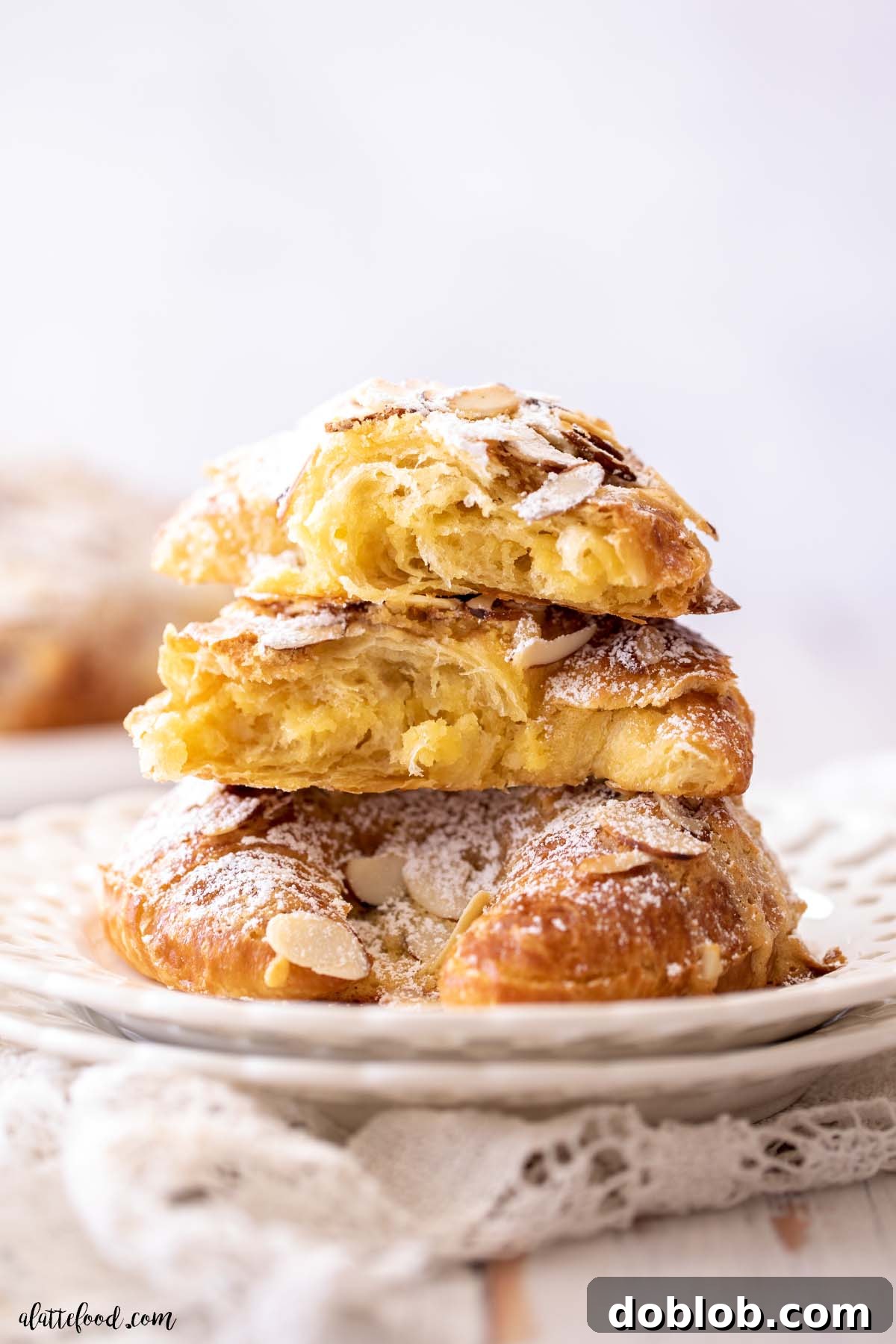 These easy Almond Croissants are one of my favorite pastry recipes! Made with day old croissants and filled with an almond frangipane, these are flaky and buttery and perfect. Almond Croissants with sliced almonds and almond paste on a white plate. A perfect pastry.