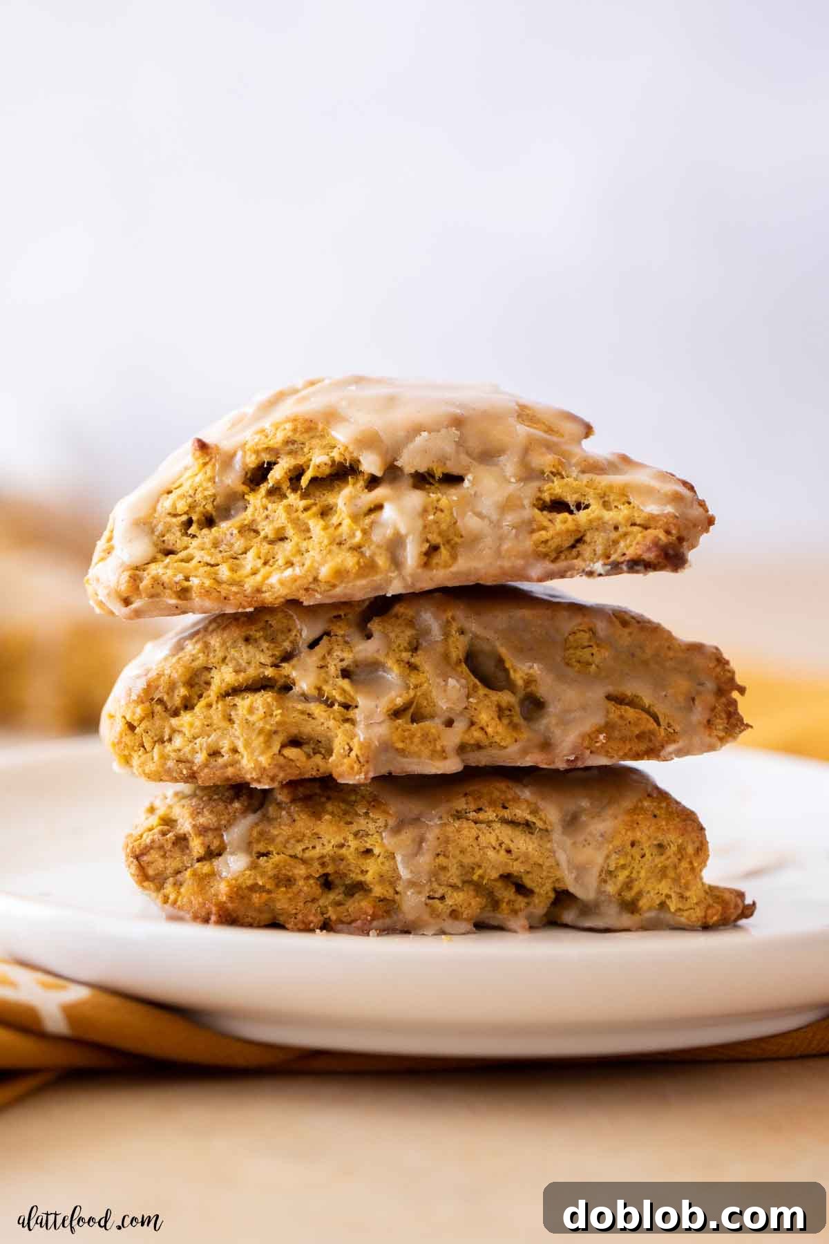 Learn how to craft the most exquisite pumpkin scones from scratch, boasting a tender crumb and delightful maple glaze. A captivating stack of buttermilk pumpkin scones, beautifully presented on a pristine white plate, promising deliciousness.