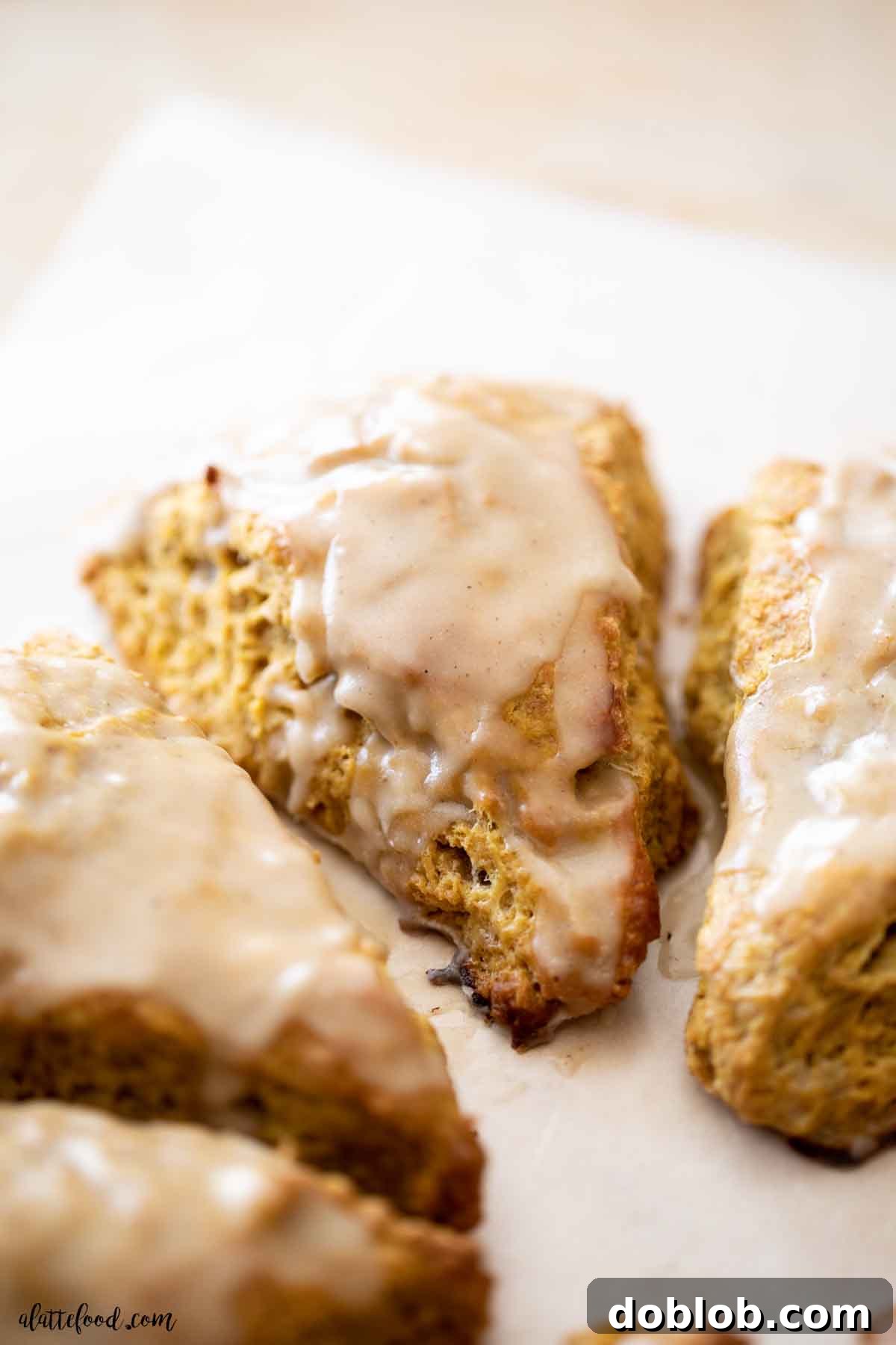 Autumn Spiced Pumpkin Scones with Maple Drizzle 3 maple glazed pumpkin scones on parchment paper.