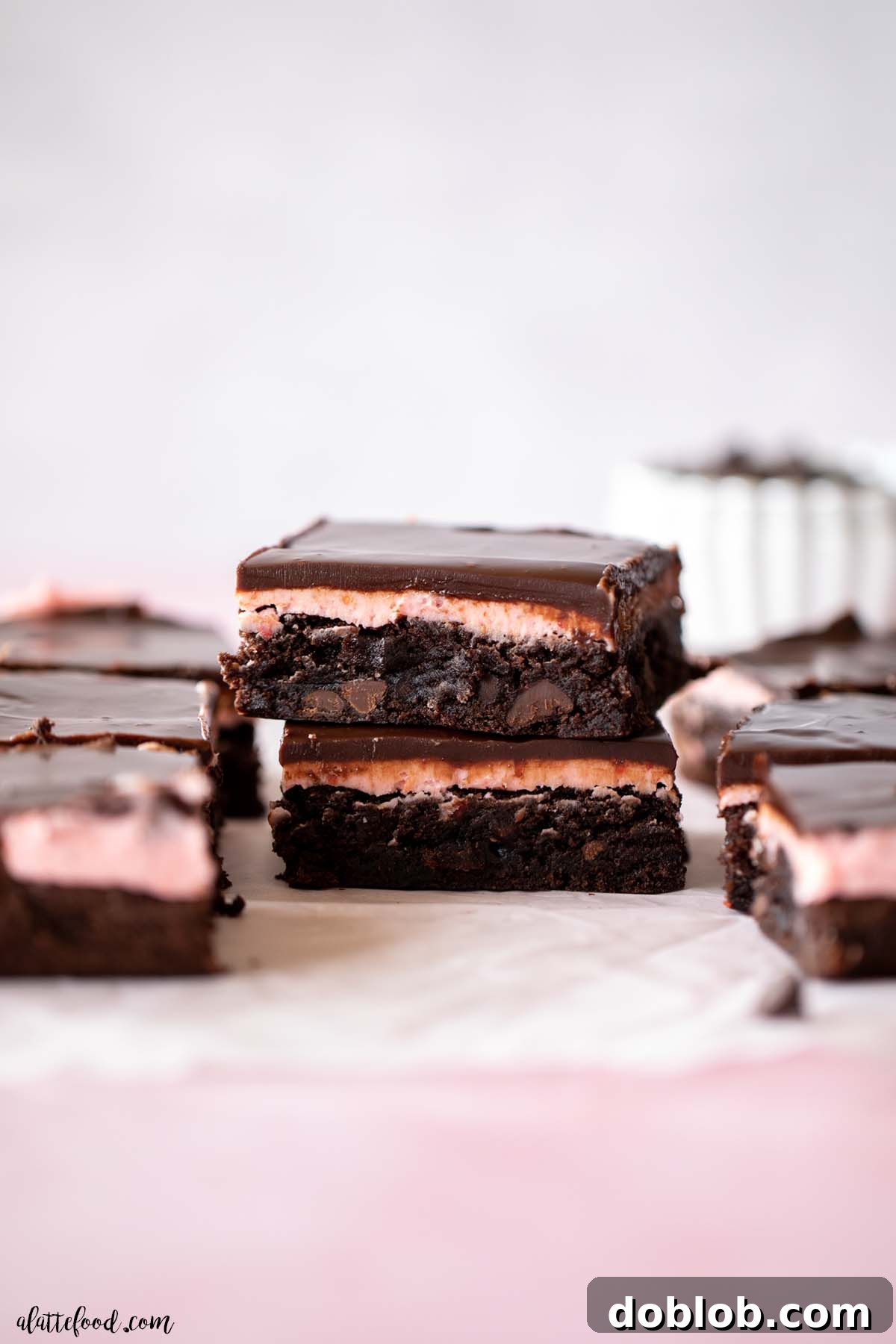 Chocolate Brownies topped with strawberry buttercream and rich chocolate ganache stacked on top of each other on parchment paper.