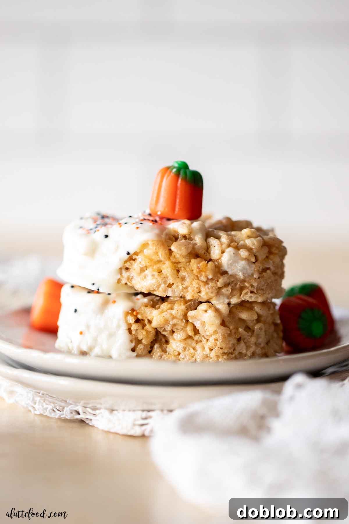 Two pumpkin spice rice krispie treats, elegantly dipped in white chocolate, stacked with a charming pumpkin candy corn on top. A festive treat for fall celebrations.