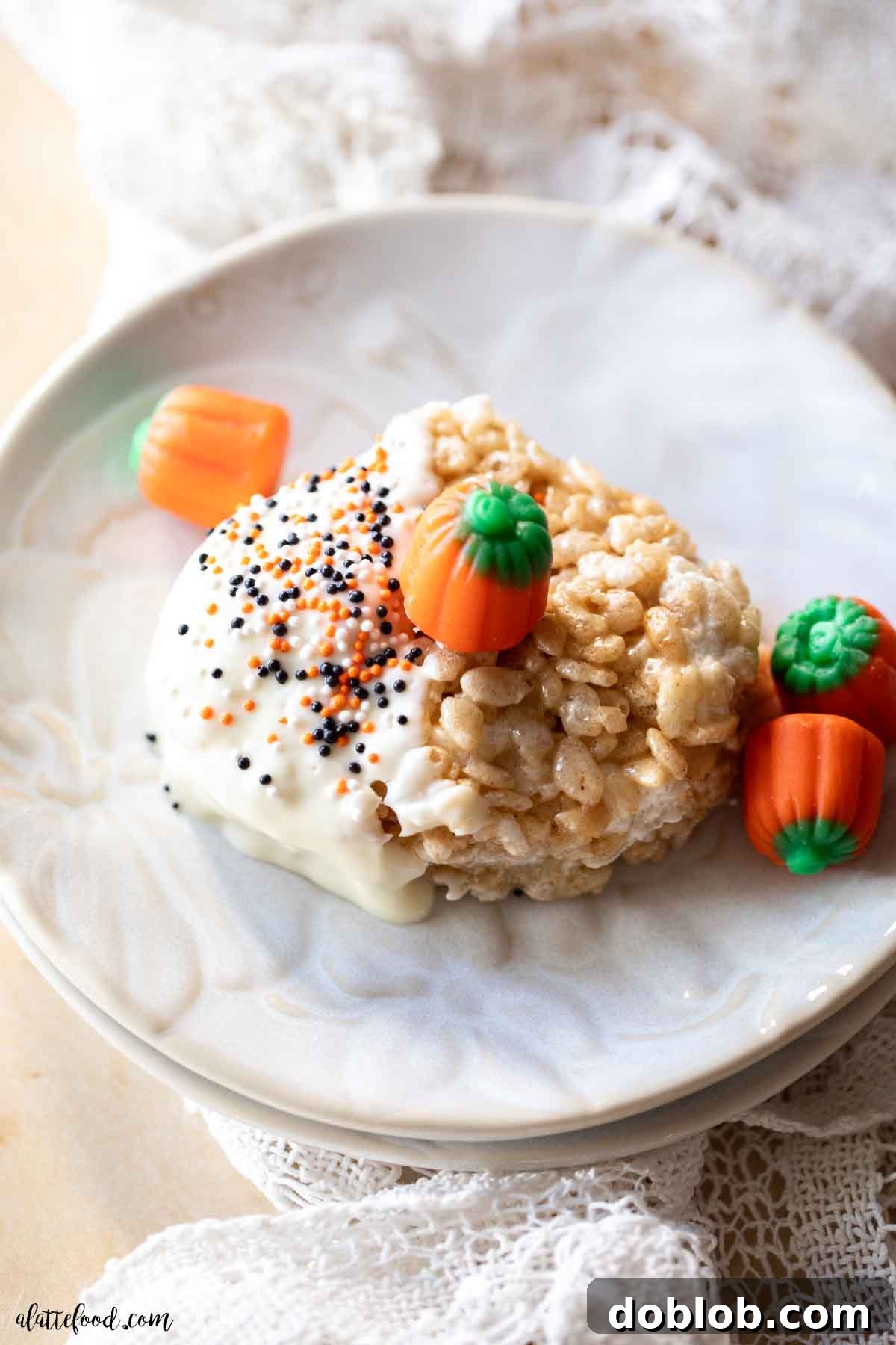 A single pumpkin-shaped pumpkin spice rice krispie treat, beautifully dipped in white chocolate, presented on an elegant white pumpkin plate. An easy, festive fall dessert.