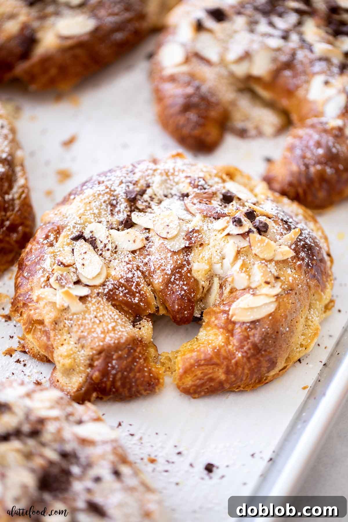 Powdered sugar covered chocolate almond cream filled croissants on metal baking tray.