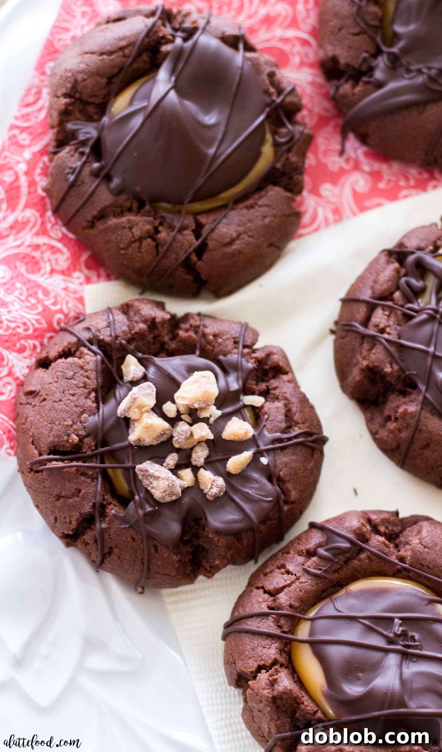 A close-up shot of several chocolate caramel thumbprint cookies, beautifully decorated with chocolate drizzles.