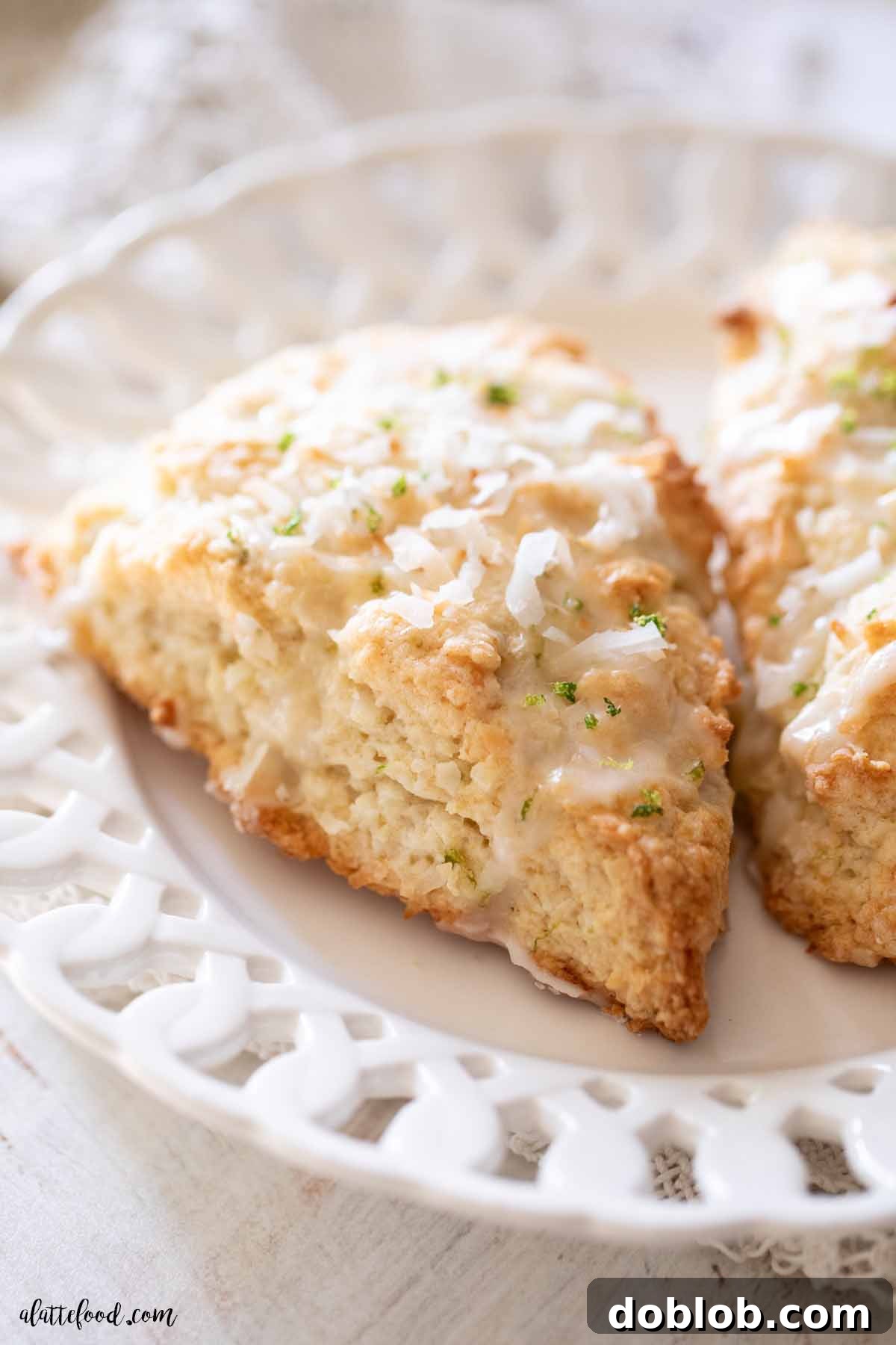 Flaky coconut lime scones with golden toasted coconut and a bright lime glaze, arranged on a pristine white plate.