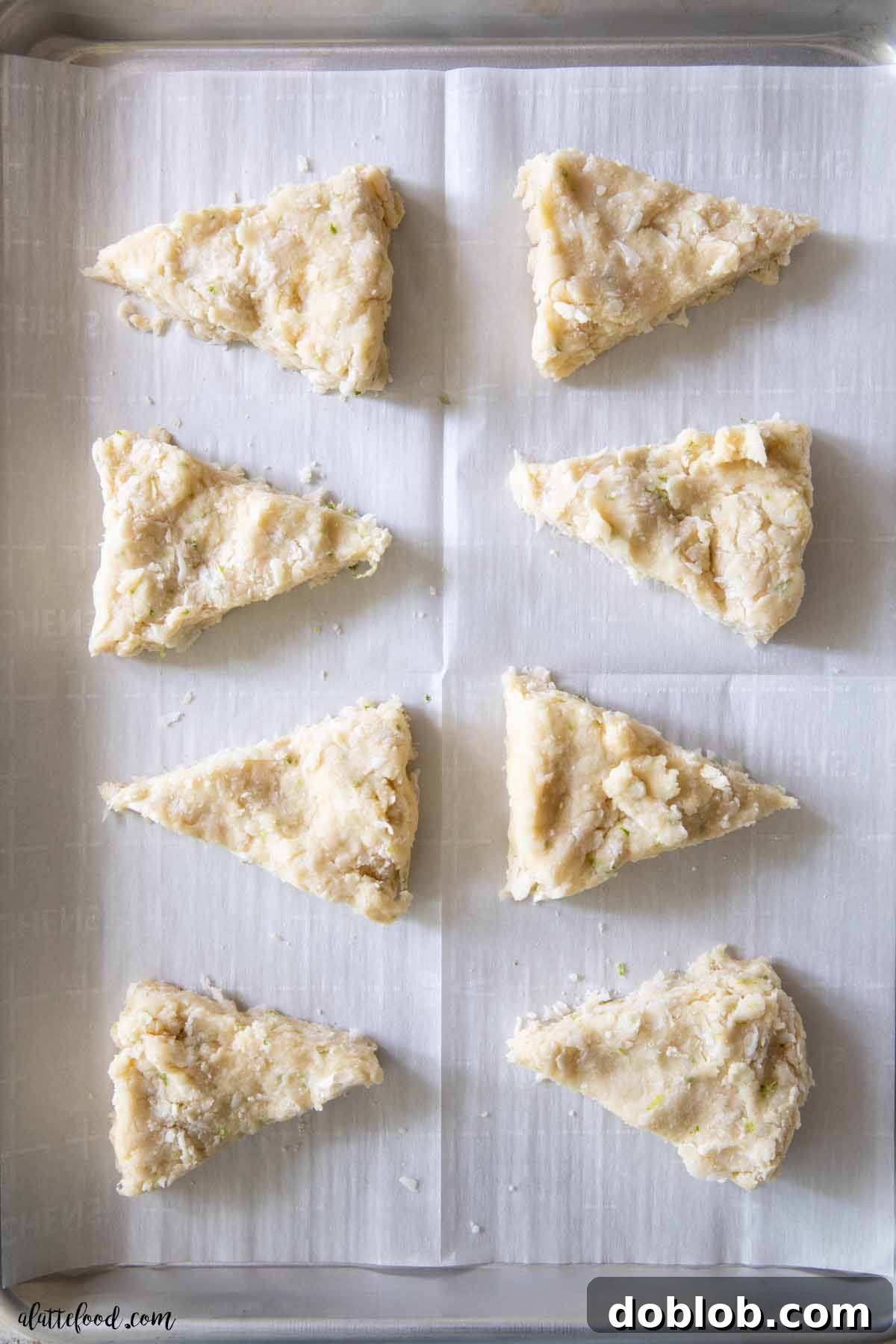 Unbaked coconut lime scones, perfectly cut into triangles, resting on a parchment-lined baking sheet, ready for the oven.