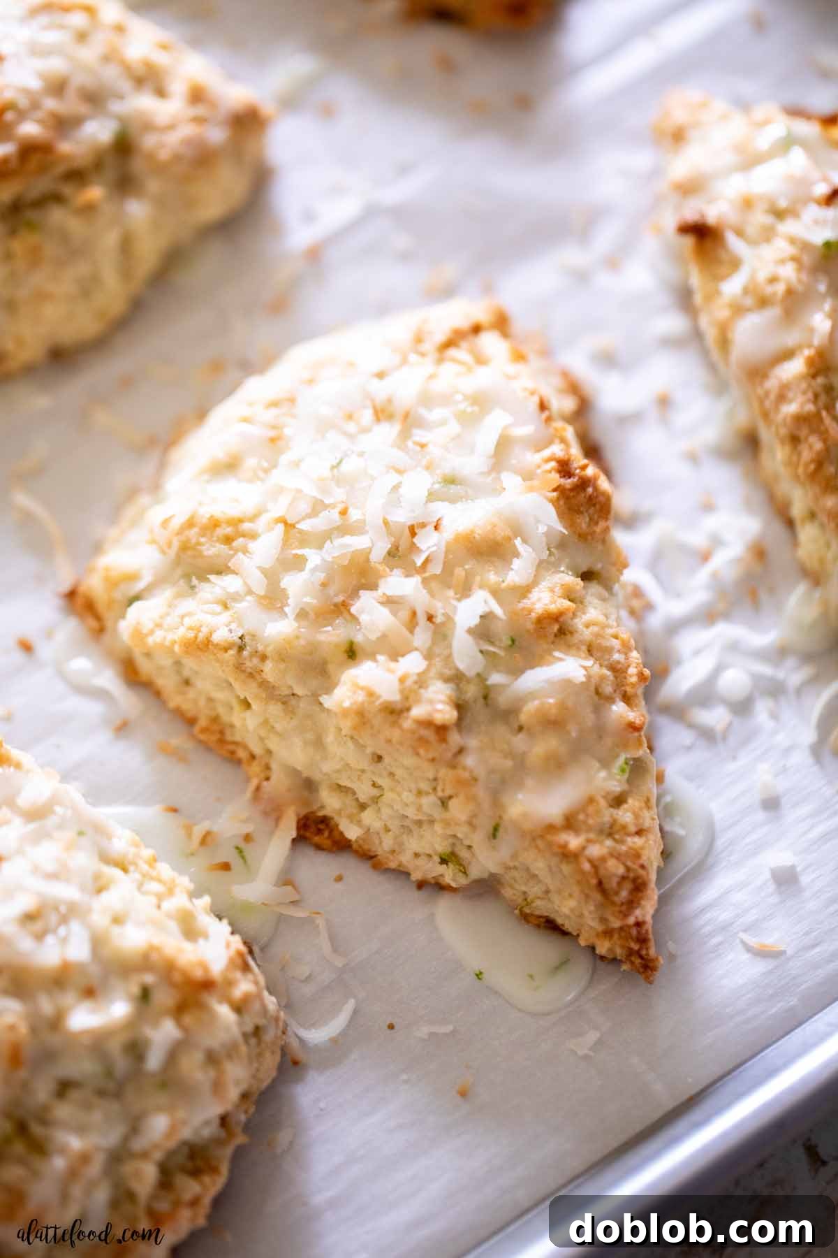 A freshly baked coconut lime scone, glistening with a vibrant lime icing, showcased on brown parchment paper.