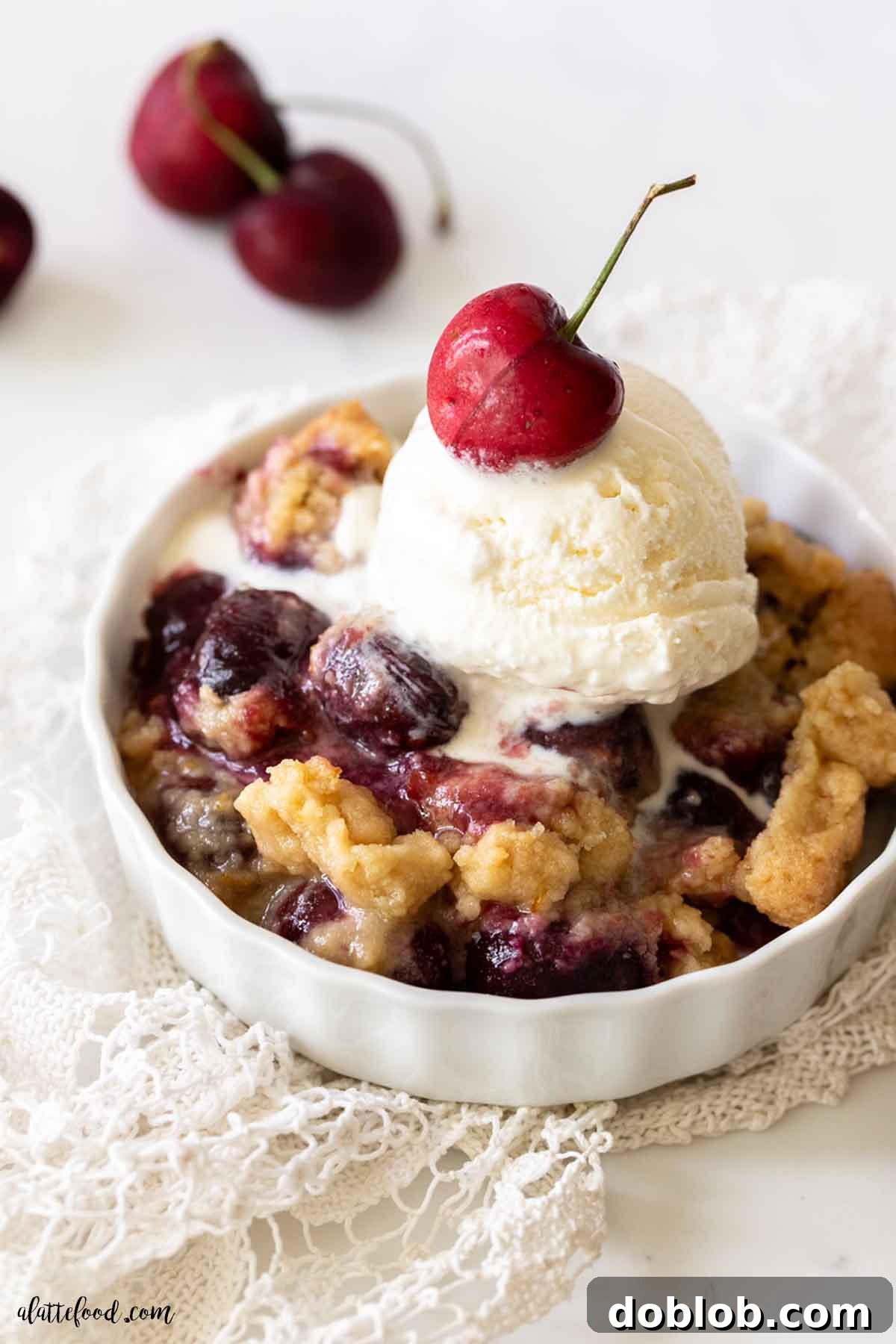 An easy cherry crumble, made with fresh or frozen cherries, topped with crisp and buttery crumble and ice cream. Warm cherry crumble with a scoop of vanilla ice cream on top in a white bowl, ready to be enjoyed.