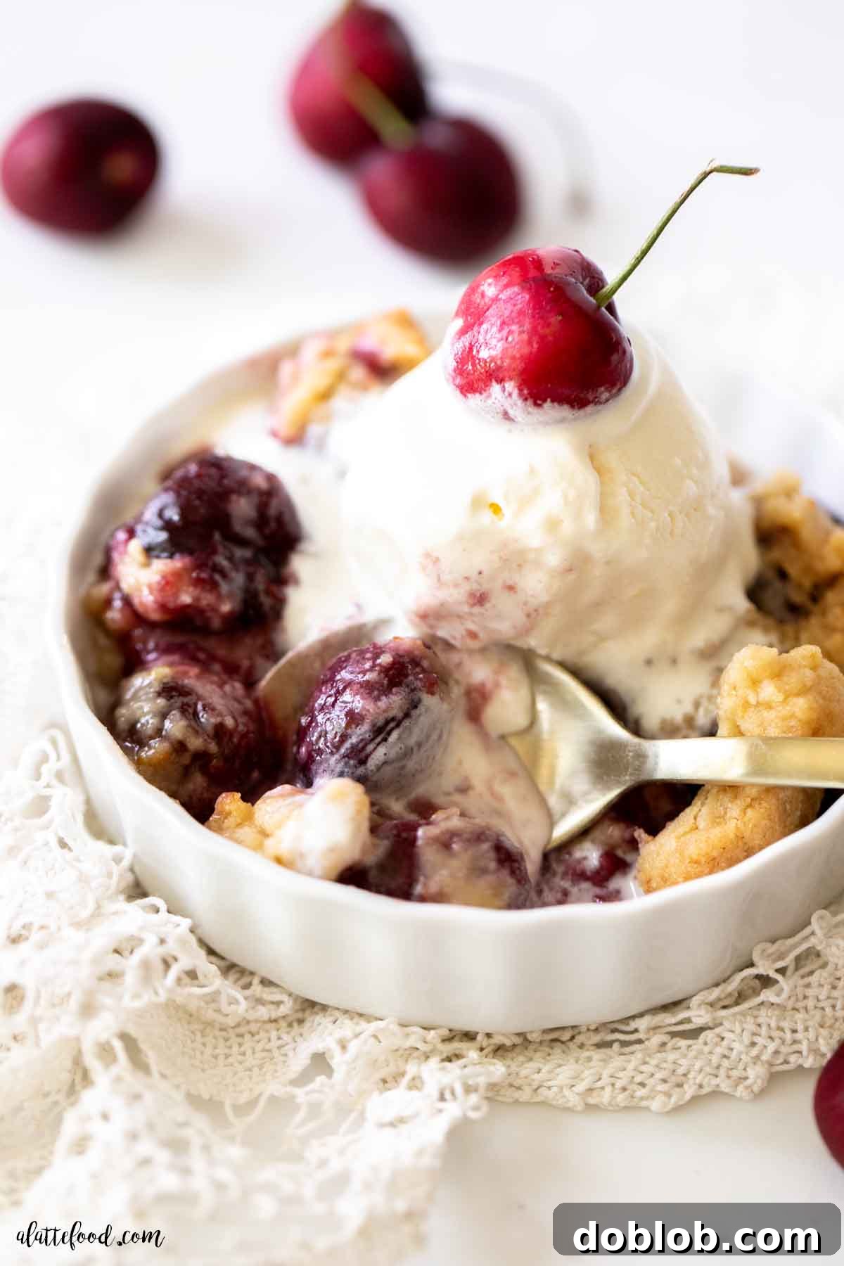 Homemade old-fashioned Cherry Crumble with fresh summer cherries, a shortbread-like crumb topping, and a scoop of vanilla ice cream. Warm cherry crumble in a white ramekin with a spoon scooping the cherry filling, showing the rich texture.