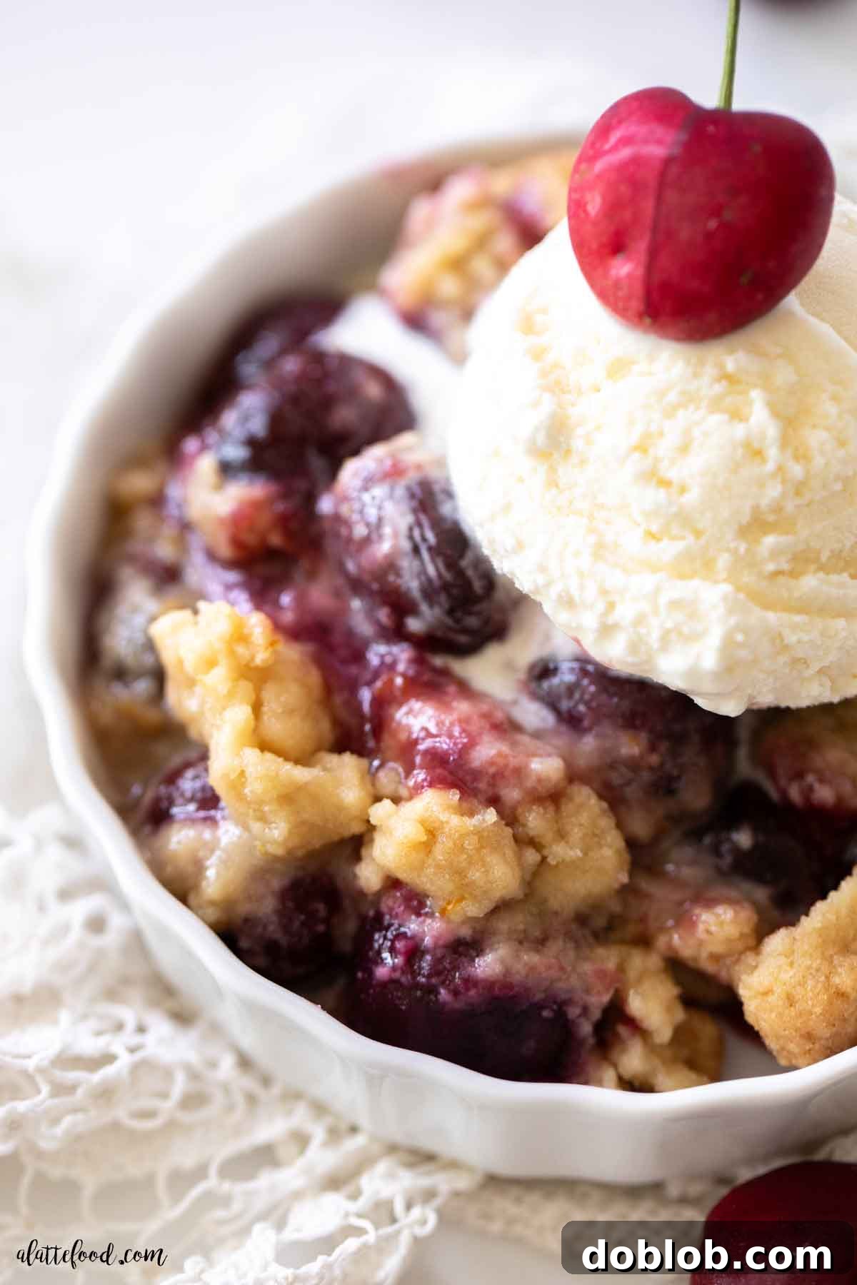 Close up of warm cherry crumble with vanilla ice cream melting on top of the cherry cobbler filling in a white bowl.