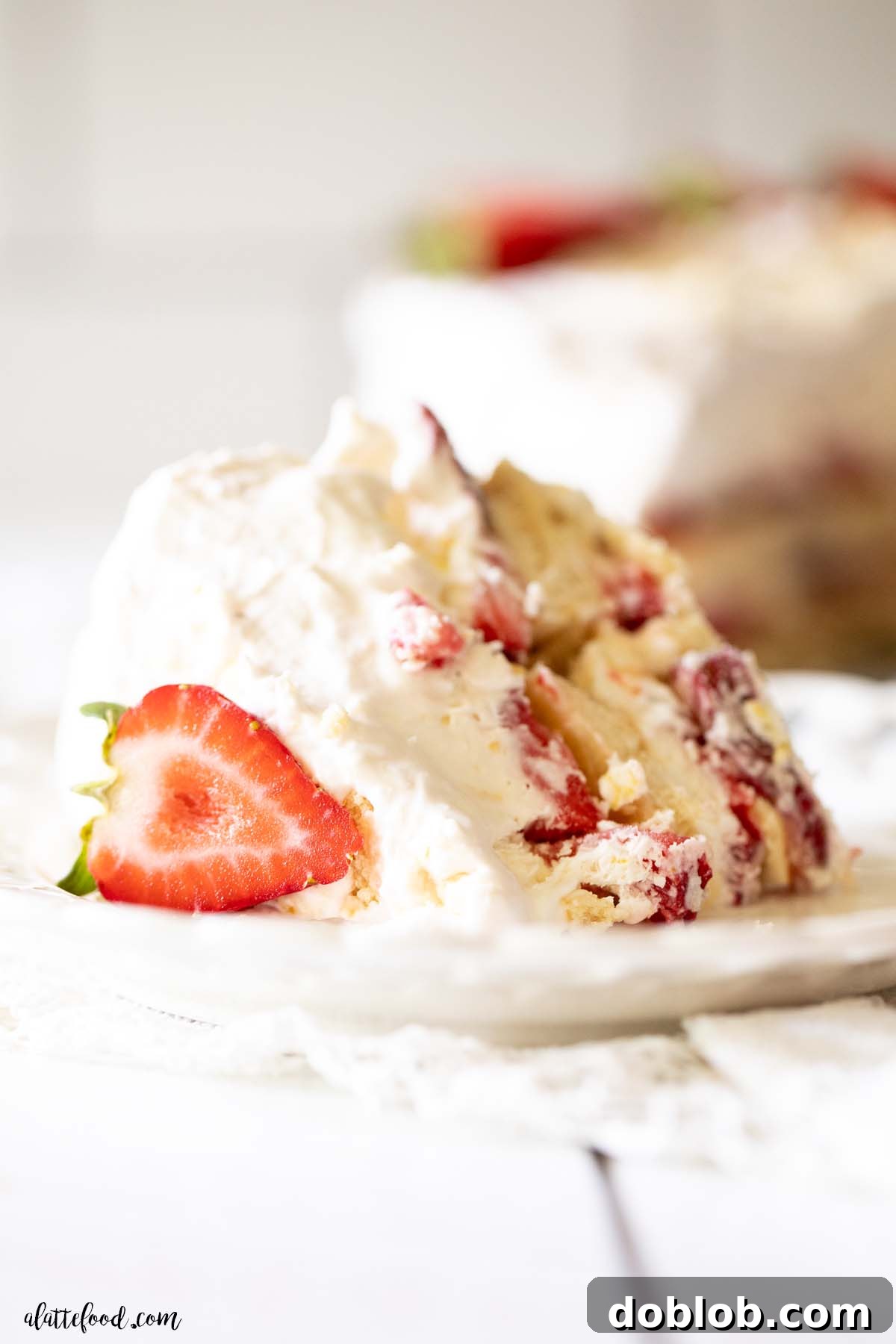 strawberry lemon whipped cream cake sliced with fresh strawberries and on a white plate.