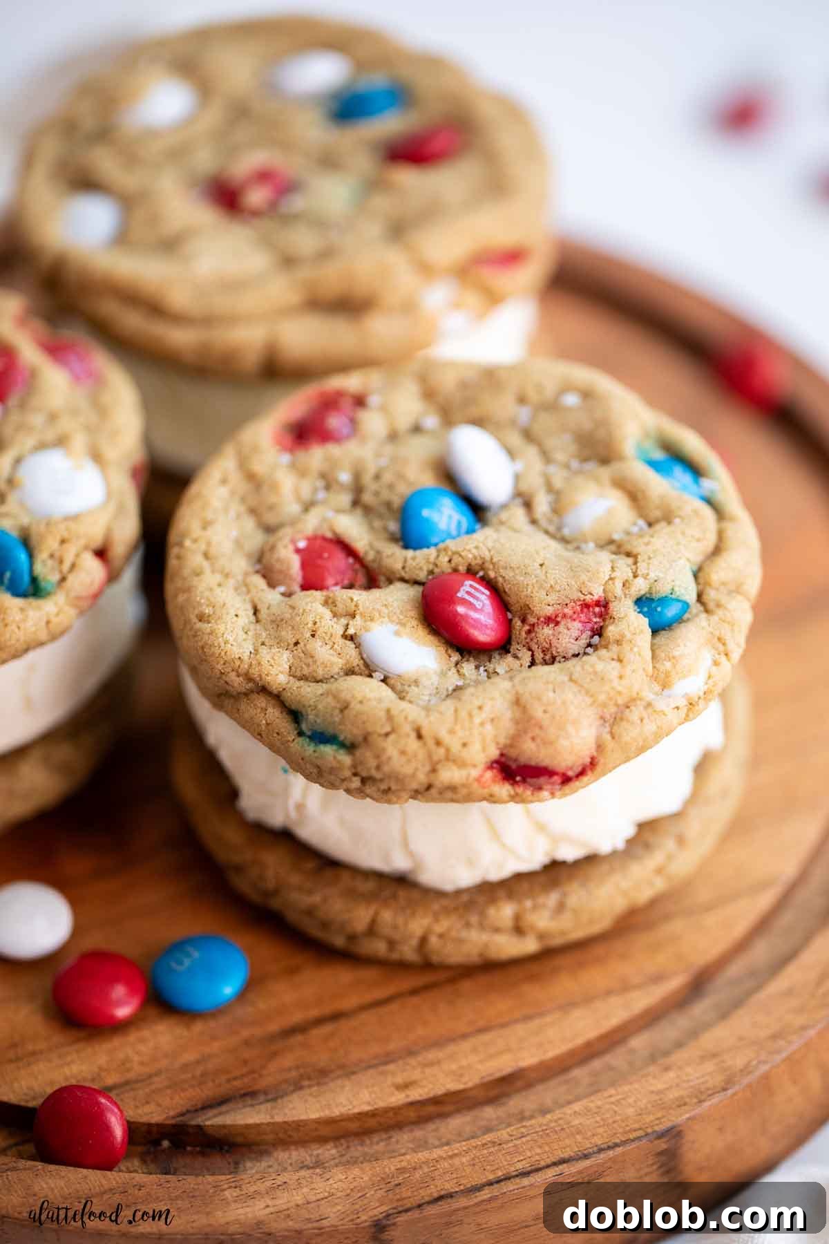 Stacked vanilla M&M cookie ice cream sandwiches on a wooden cake stand, highlighting the creamy vanilla filling and colorful M&M cookies.