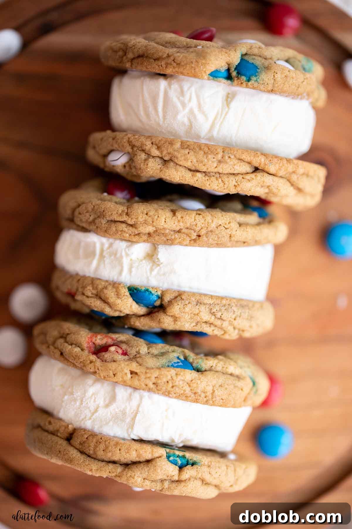 Three perfectly stacked M&M ice cream sandwiches with creamy vanilla ice cream, arranged on a rustic wood board, ready to be enjoyed.
