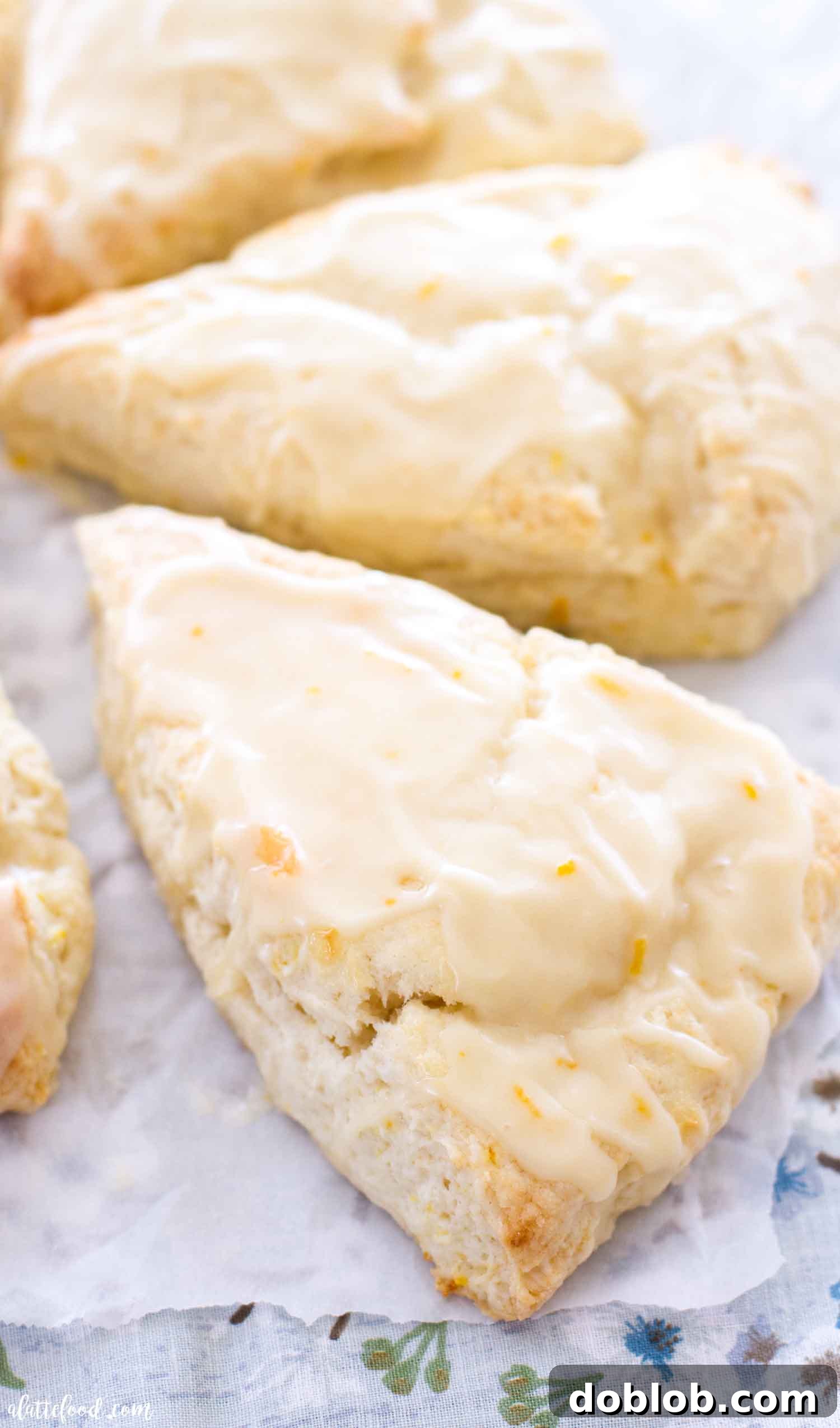 Dreamsicle Orange Cream Scones 3 Triangular orange scones with glistening orange glaze on parchment paper