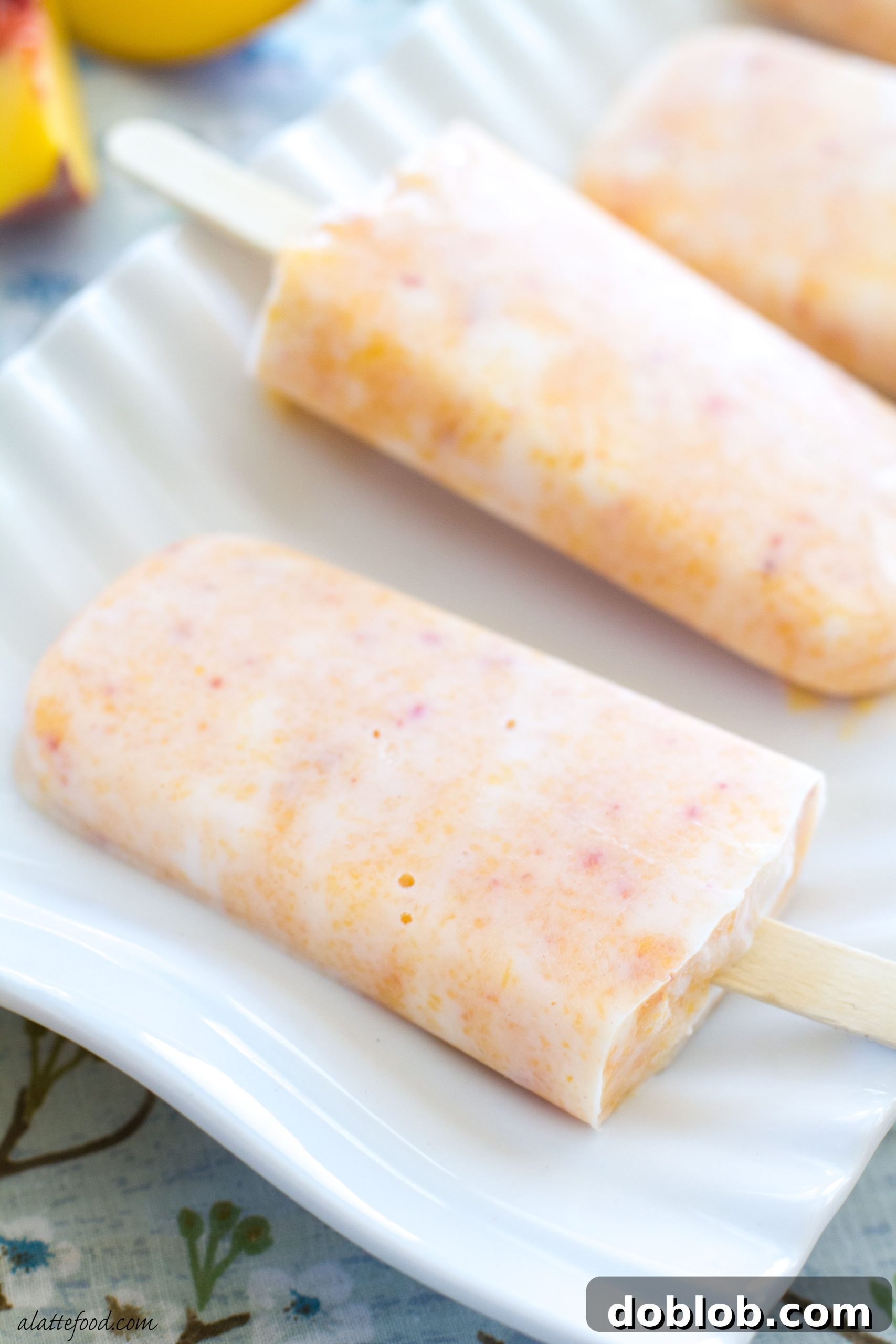 A hand holding a creamy peach popsicle, ready to take a bite, emphasizing its refreshing appeal