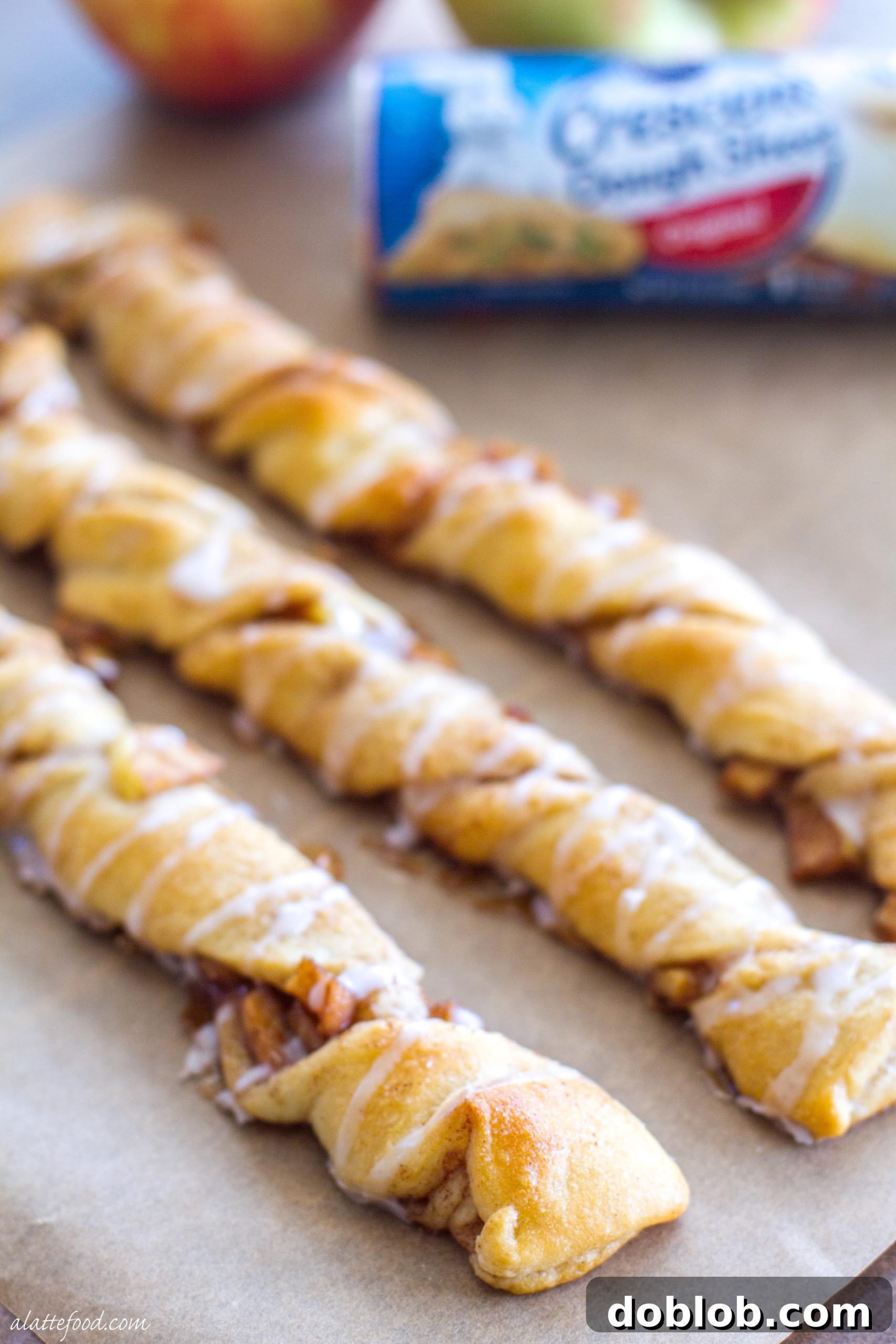 A close-up of a single apple danish twist on a wooden surface, highlighting the glaze and texture