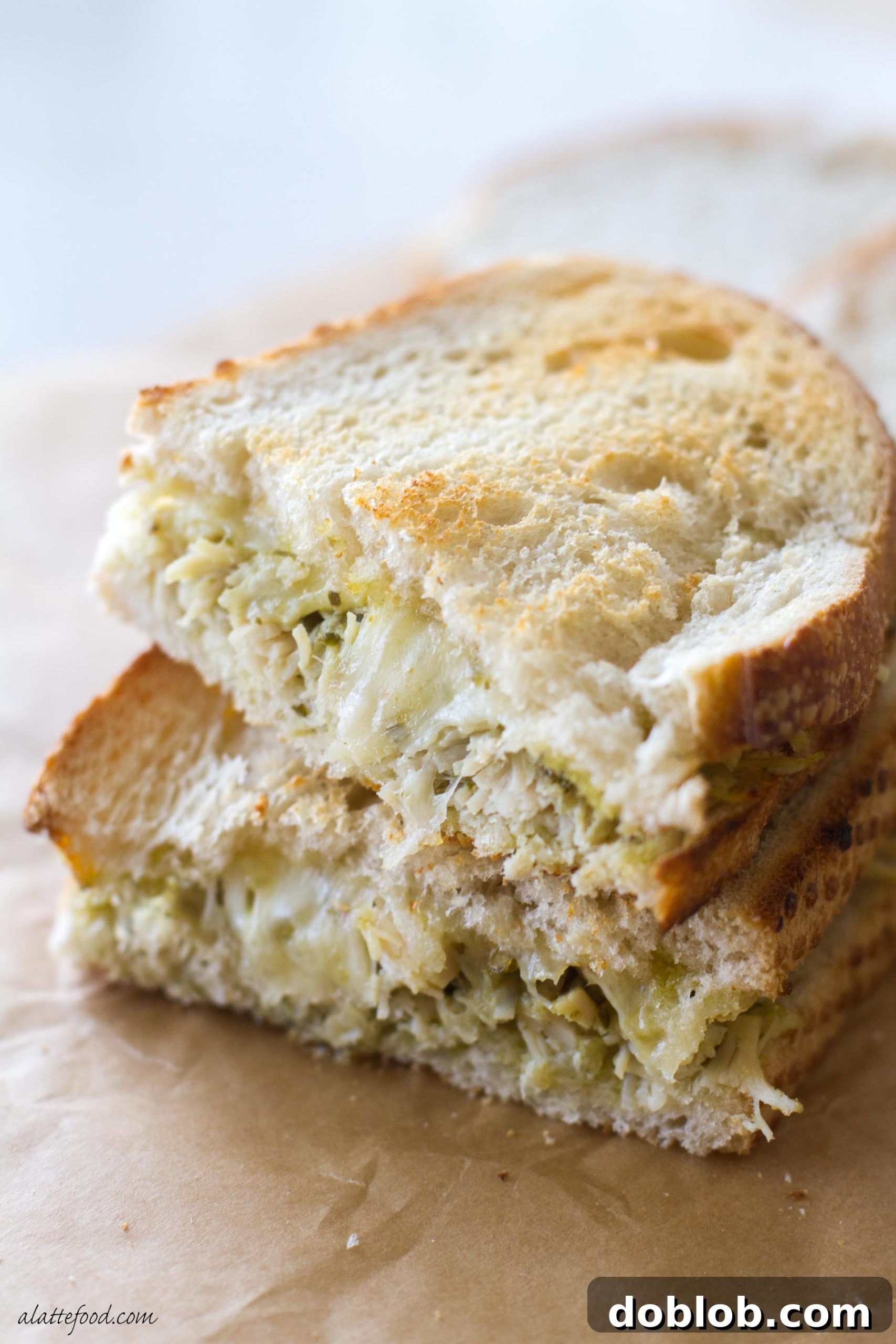 Gourmet Pesto Tuna Melt 2 Two halves of a perfectly golden-brown pesto tuna grilled cheese sandwich, showing the melted white cheddar cheese and a hint of green pesto and tuna filling.