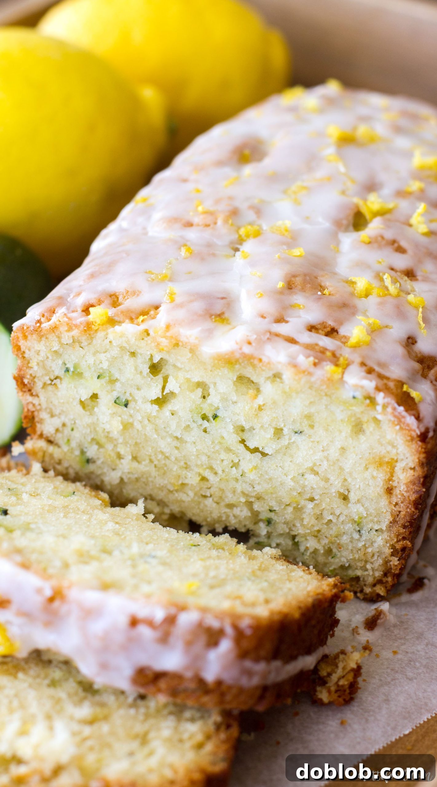 A close-up of a freshly baked lemon zucchini bread loaf, ready for slicing, emphasizing its golden-brown crust and lemon glaze.