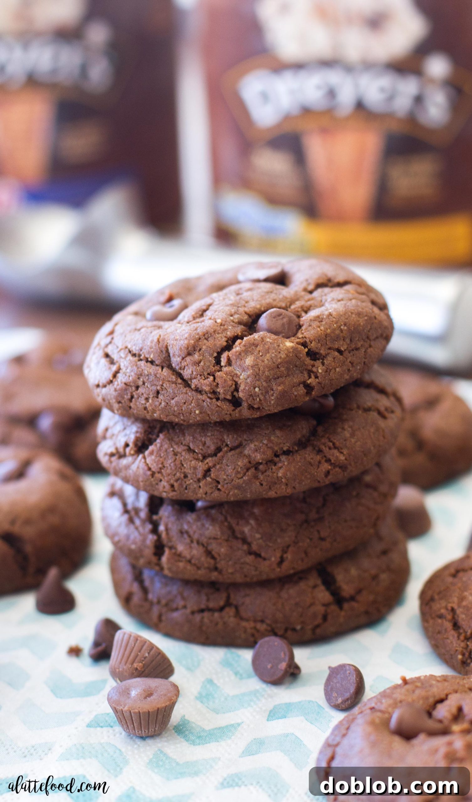 Stacked double chocolate peanut butter caramel cookies, with some candies and peanut butter chips scattered around
