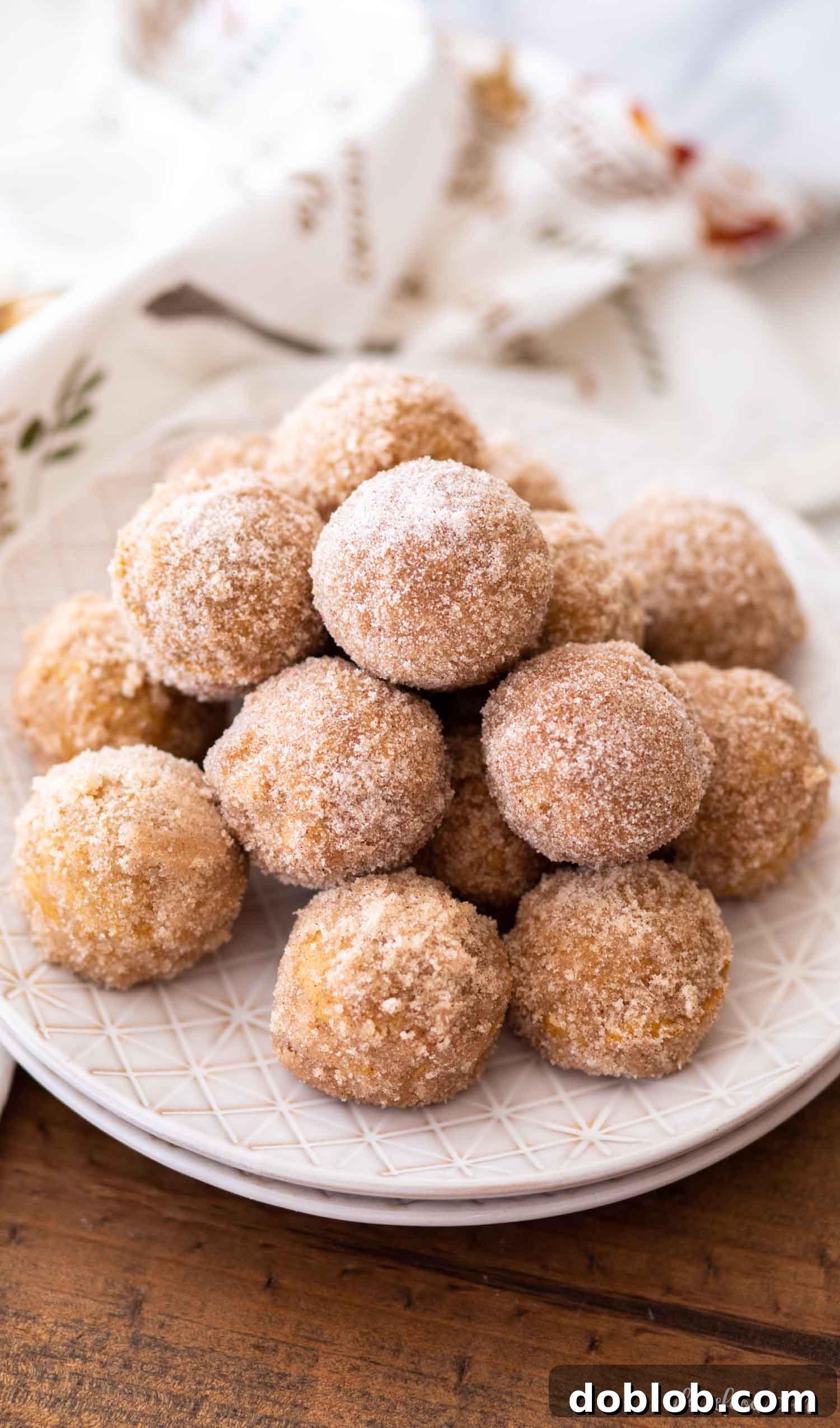 A stack of golden pumpkin donut holes, generously coated in cinnamon sugar, resting on plates.