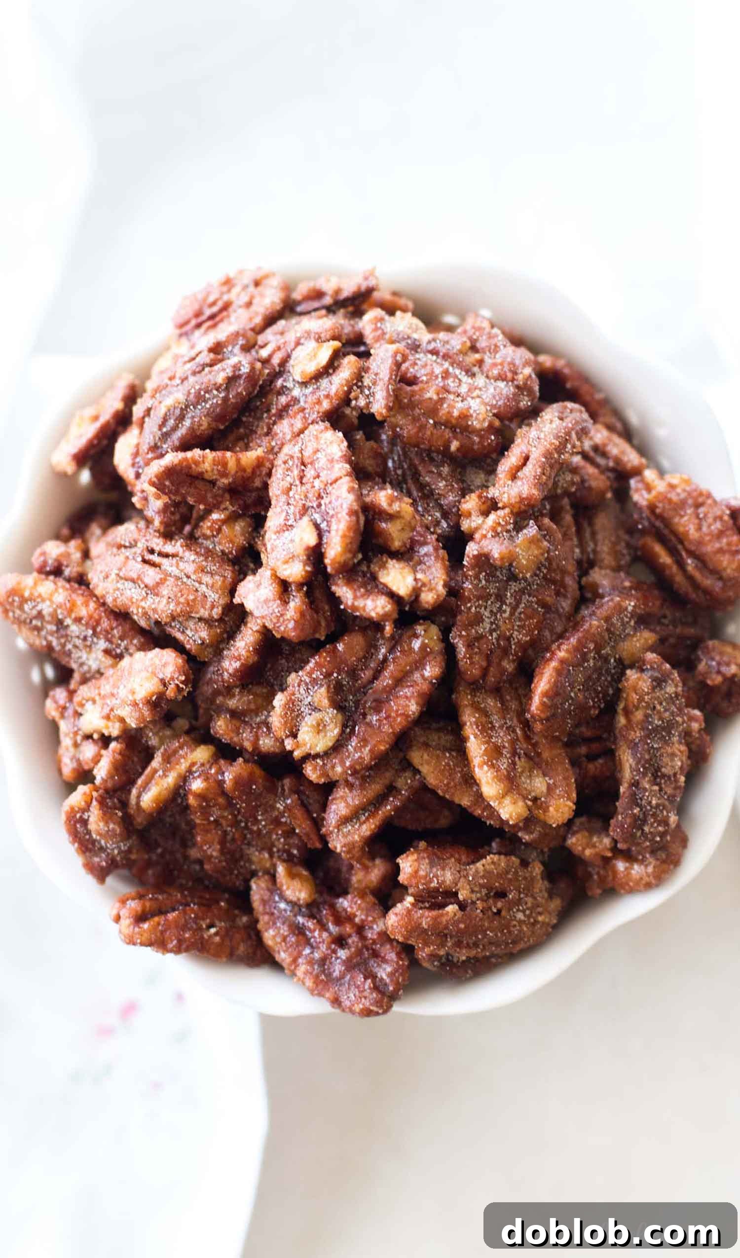 Perfectly coated maple candied pecans arranged on a white cutting board, beside a rustic white dish towel, highlighting their irresistible texture.