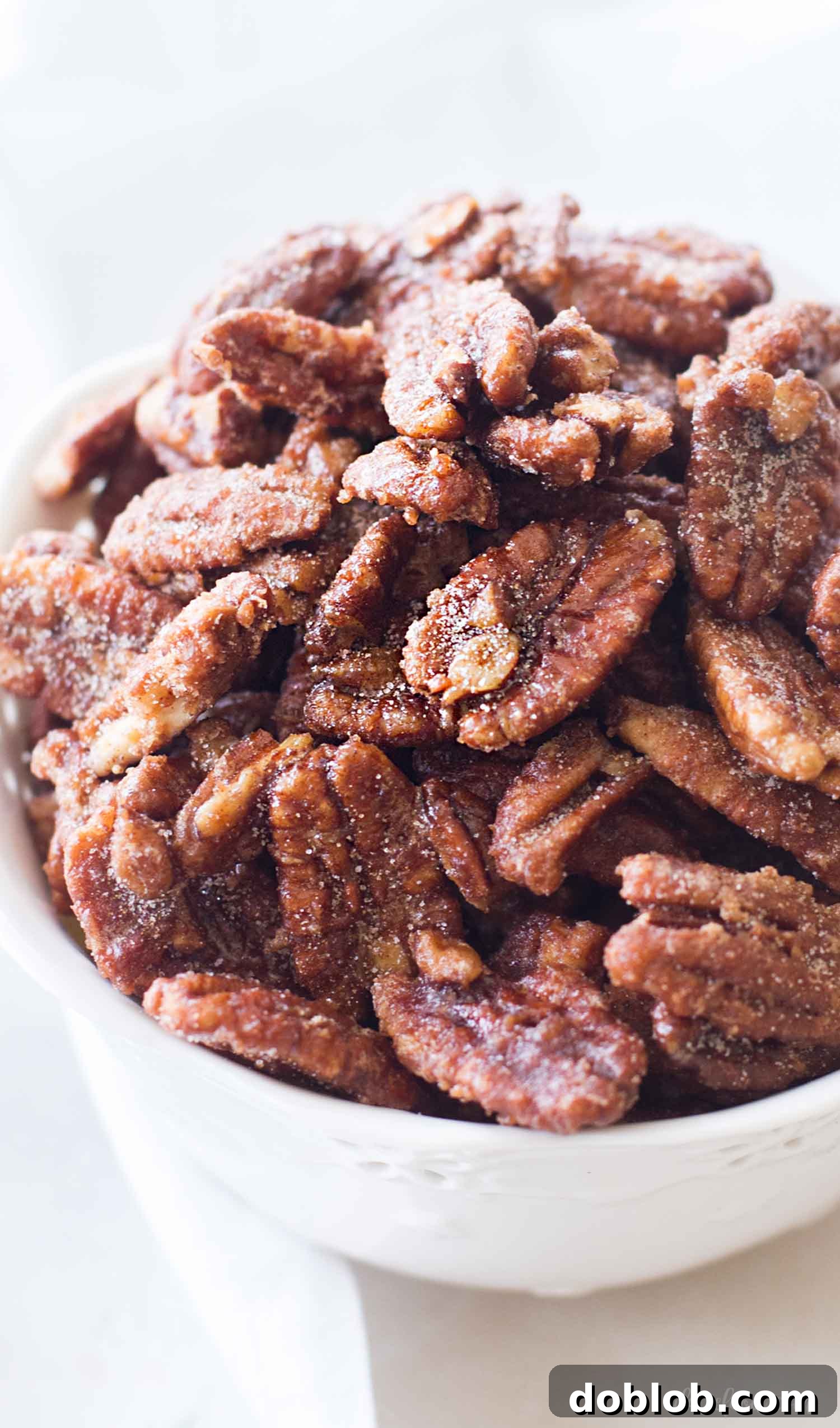A close-up of maple candied pecans nestled in a white bowl, highlighting their rich, glossy coating and inviting texture.