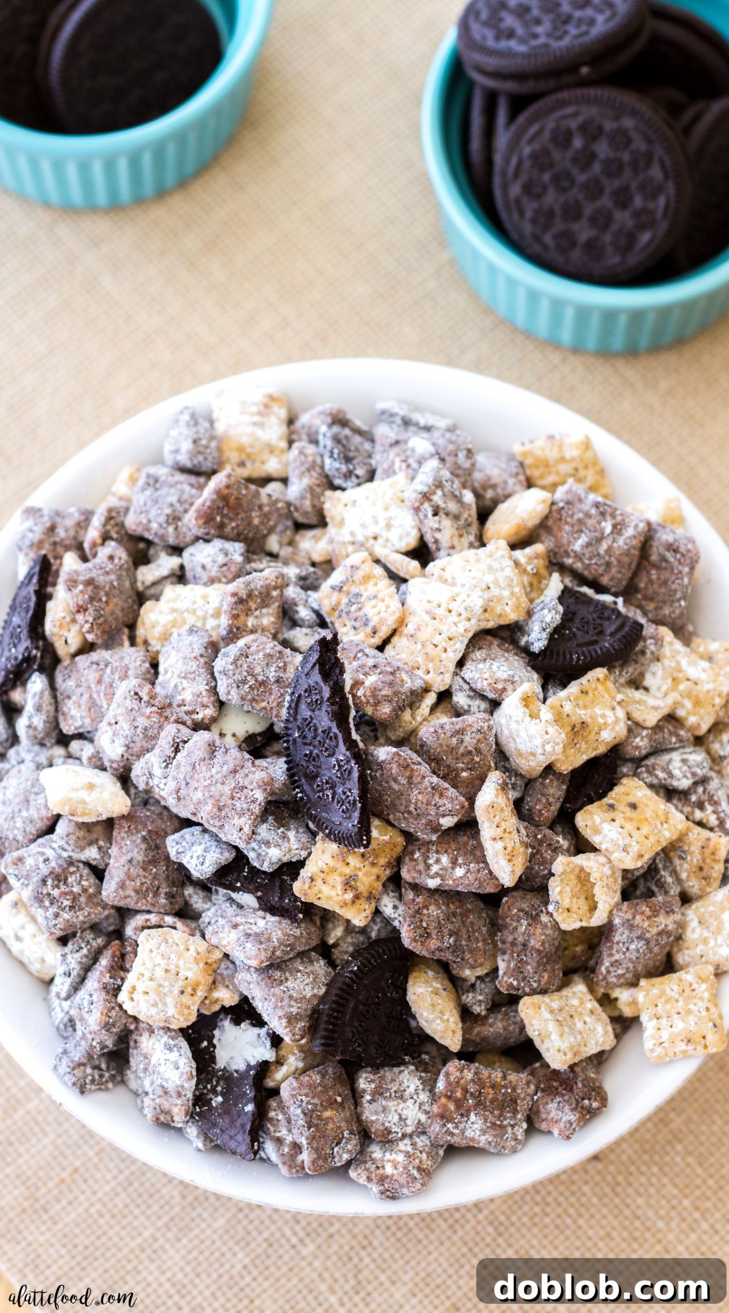 Close-up of a bowl filled with Salted Caramel Cookies 'n Cream Puppy Chow, dusted with powdered sugar and Oreo crumbs.