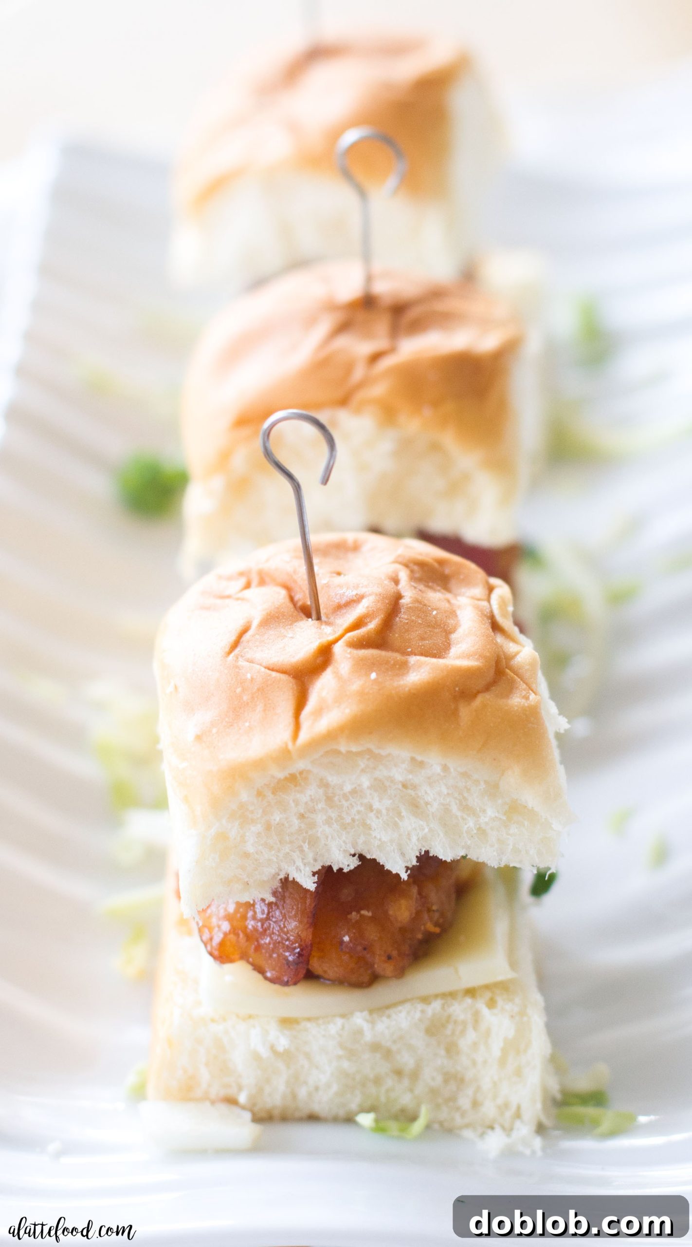 Individual bacon wrapped chicken sliders with melted cheese and fresh cabbage on soft rolls