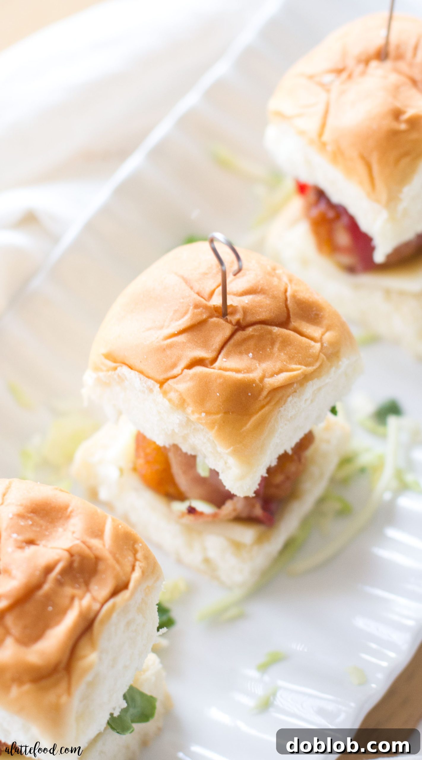Spread of finished bacon wrapped chicken sliders on a white serving platter, garnished