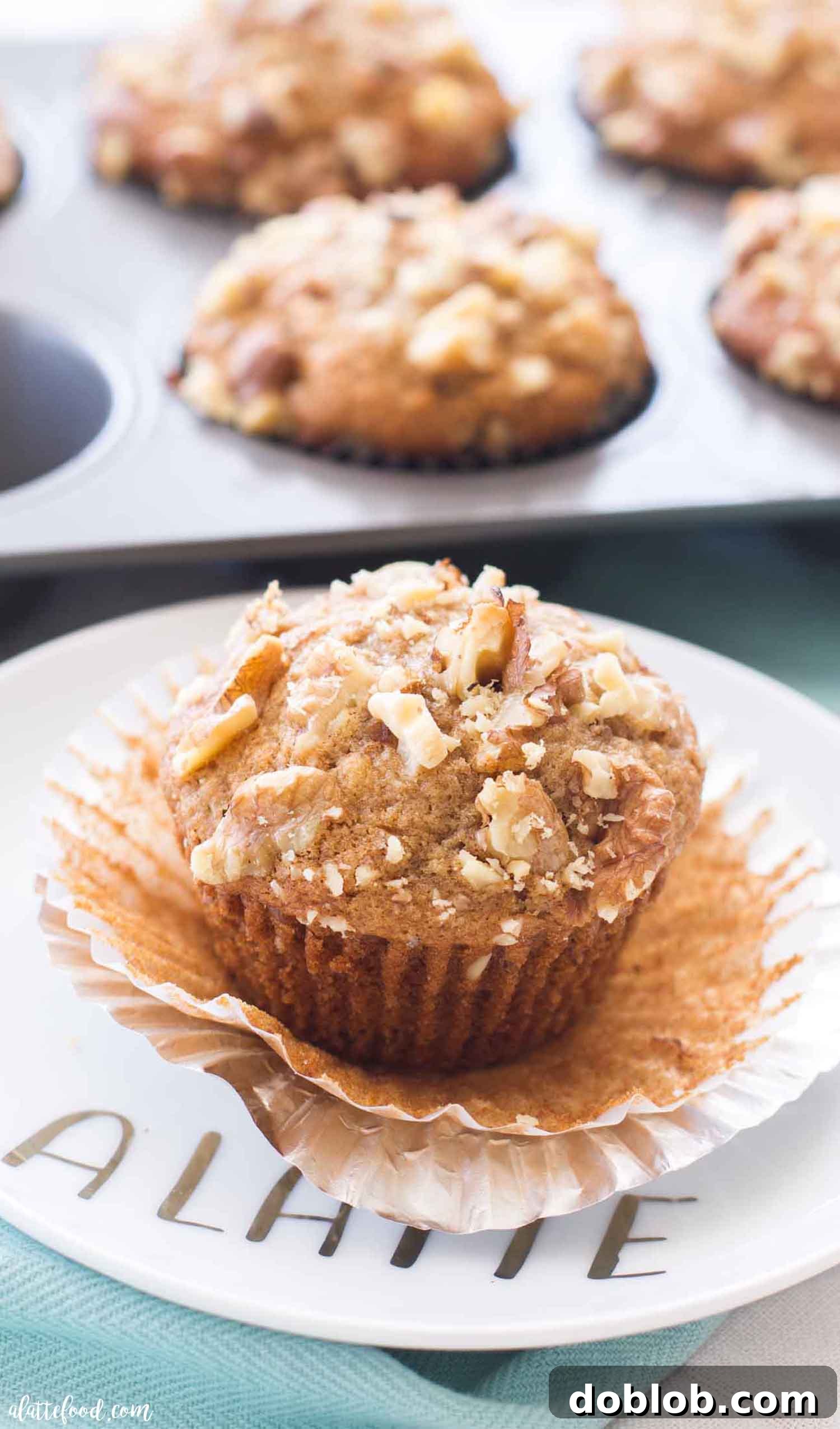 If you love banana bread, then you are sure to love these Banana Nut Muffins! They are light and fluffy in texture and incredibly moist thanks to the mashed ripe bananas. They have a healthy dose of walnuts on top, but you can easily make these nut free banana muffins too! #breakfast #banana #muffin #recipe A perfectly baked banana nut muffin, unwrapped and ready to enjoy on a white plate. It showcases its golden-brown top and visible walnut pieces, highlighting its moist and fluffy interior.
