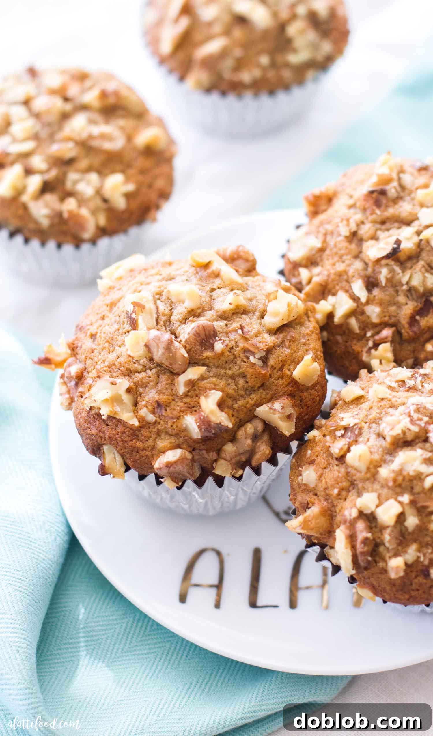 Fluffy banana muffins begin with ripe bananas that also make these banana nut muffins SO moist! Topped with chopped walnuts, these nutty banana muffins have that perfect texture of soft and crunchy. A great make ahead breakfast recipe! #banana #muffin #nut #bread #breakfast Three golden-brown banana nut muffins, artfully arranged on a pristine white plate, inviting you to grab one. The walnuts on top are clearly visible, promising a textural delight.