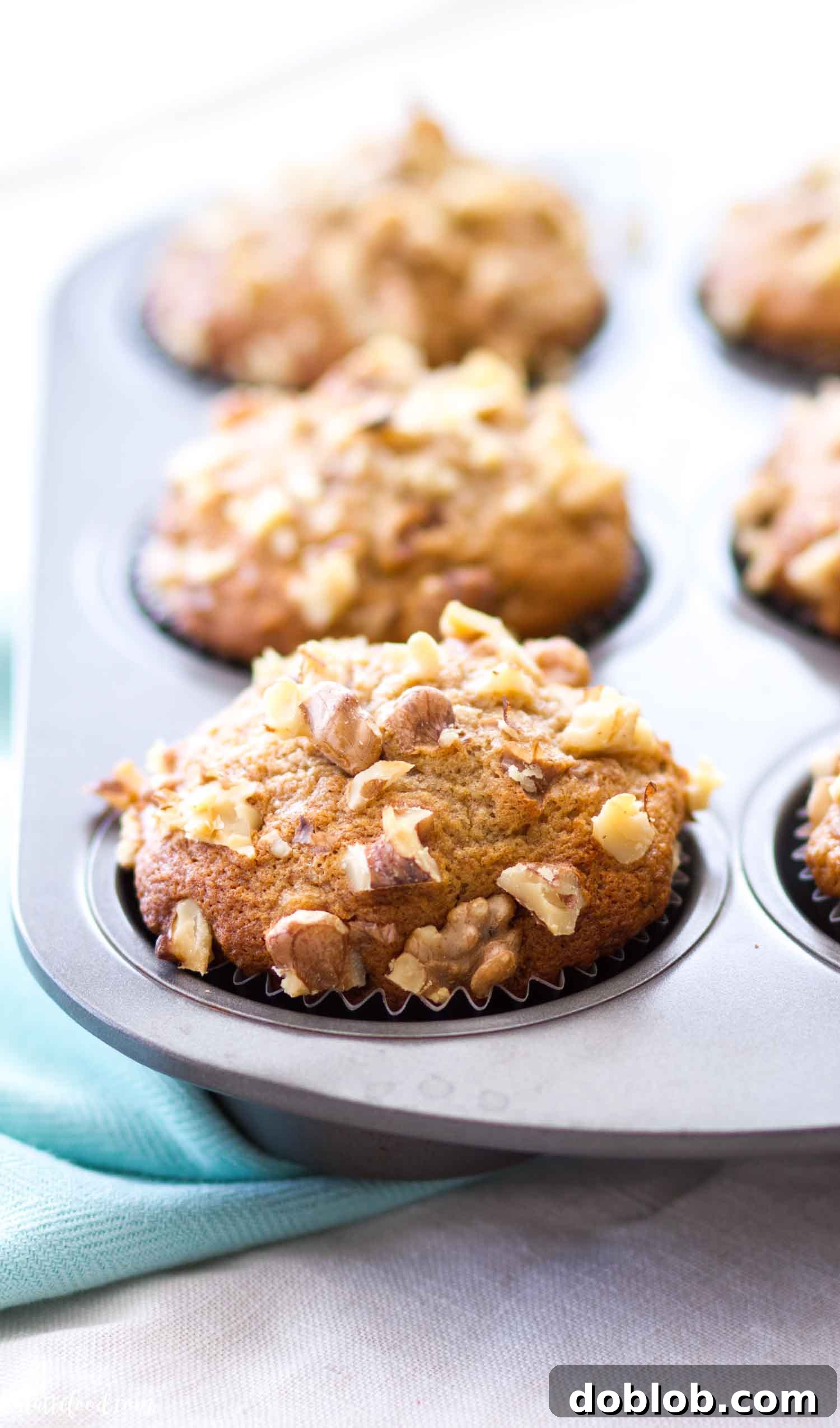 Easy Banana Nut Muffins begin with ripe bananas and end with a healthy dose of walnuts sprinkled on top! Of course, you can make these nut free or sub in any other type of nut (almonds, pecans, macadamia nuts). Plus, these banana muffins are so moist and fluffy! They make an easy breakfast or brunch, and you can make these ahead of time and freeze for later! #banana #muffin #recipe #nut #bread A muffin tin filled with freshly baked banana nut muffins, showcasing their golden domes and generously sprinkled walnuts. They look ready to be cooled and enjoyed.