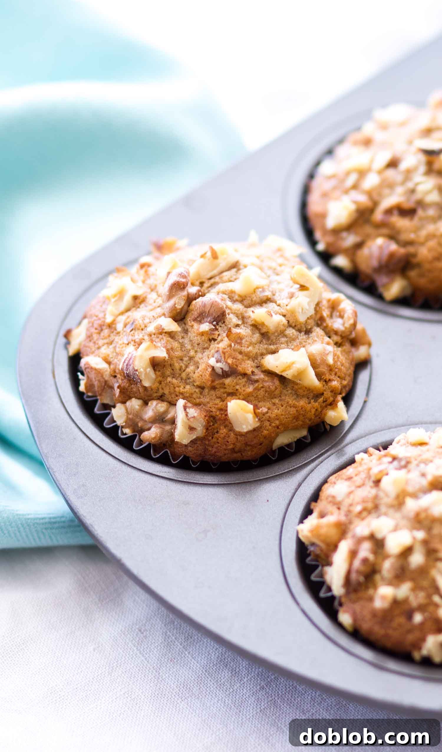 Homemade Banana Nut Muffins are so moist and fluffy! Ripe bananas are mashed and turned into these easy banana muffins topped with walnuts (you could use almonds or pecans, as well as make these nut free). They make an easy breakfast or brunch recipes! #banana #nut #muffin #bread #breakfast A close-up of several banana muffins with walnuts baked in a muffin tin, showcasing their golden-brown tops and the beautiful texture of the crumb.