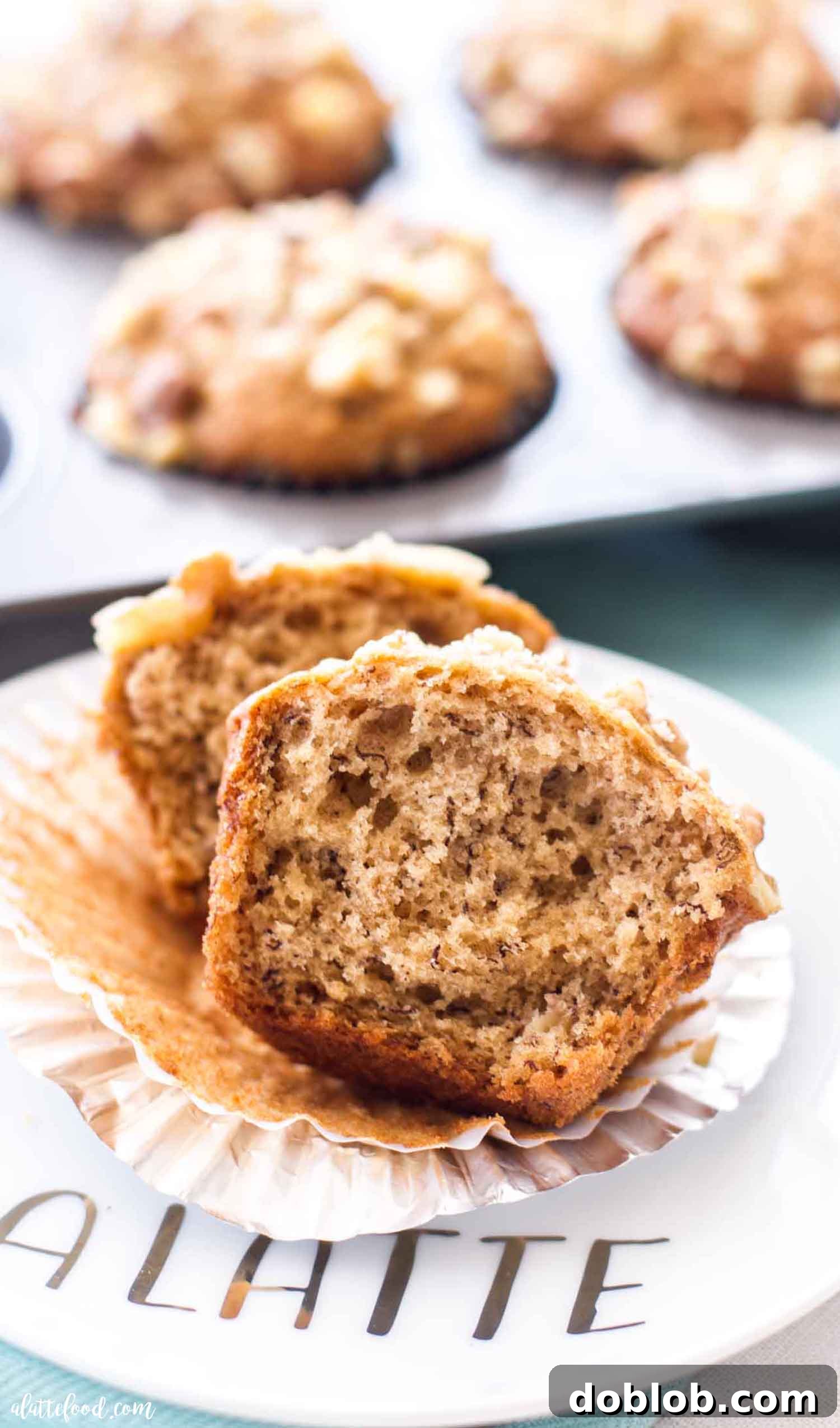 These Fluffy Banana Muffins with walnuts are one of my favorite breakfast recipes! Moist banana nut muffins are so flavorful and so easy to make, plus they can be made ahead of time and stored in the freezer for later. These Banana Nut Muffins are hearty with healthy topping of walnuts on top, but you can easily make these nut free banana muffins too! #banana #muffin #breakfast #brunch #recipe A fluffy banana muffin cut in half, revealing its moist, tender crumb and the distribution of walnuts throughout the interior. It looks incredibly appetizing.