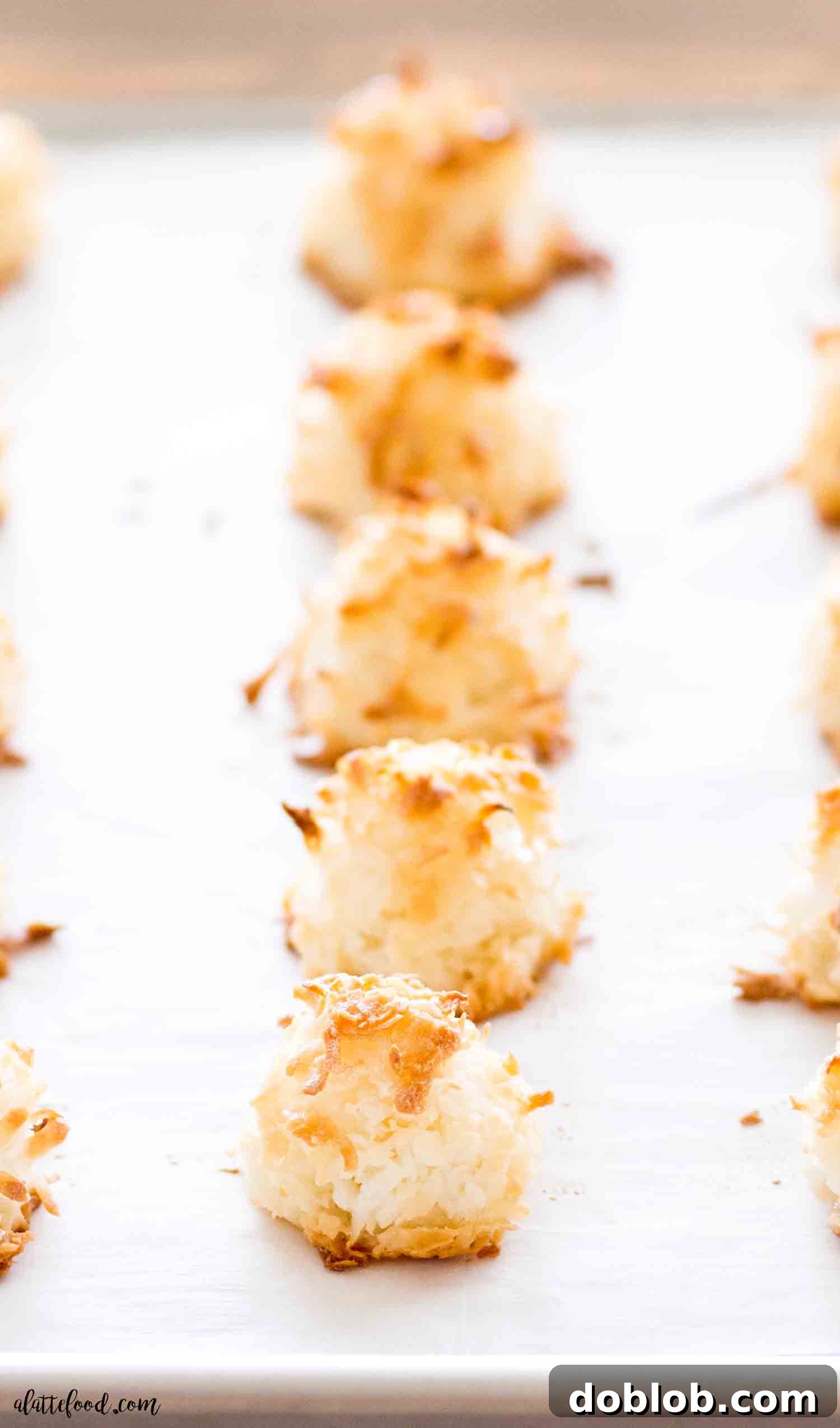 Easy homemade coconut macaroons are made with egg whites, sugar and shredded coconut. This gluten free recipe is made without sweetened condensed milk. The texture is spongy, soft and perfect. #macaroon #recipe #cookie #dessert Freshly baked homemade macaroons cooling on parchment paper, ready to be enjoyed