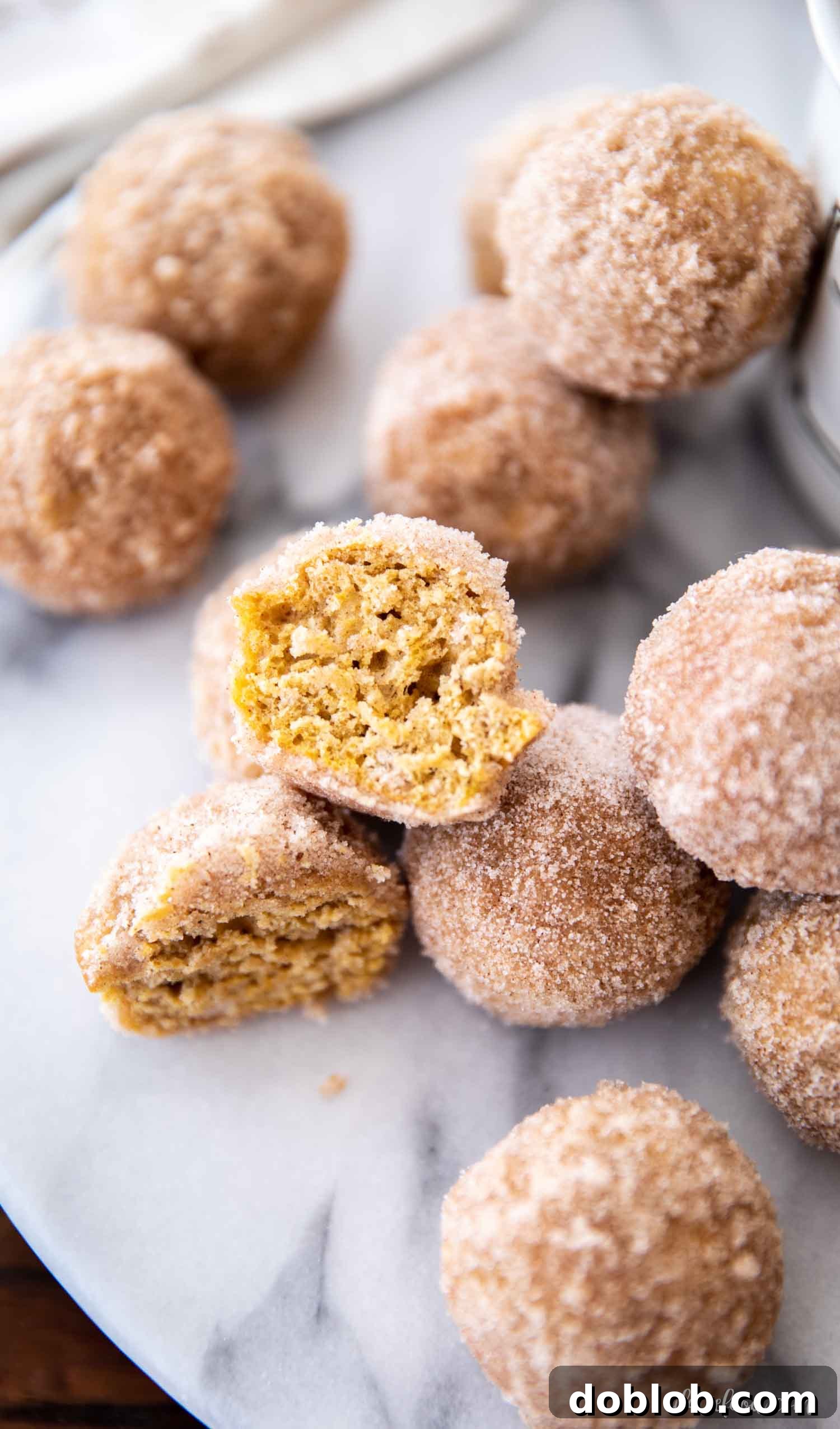 Moist Baked Pumpkin Donut Holes with Cinnamon Sugar Close-up of a baked pumpkin donut hole cut in half, revealing its moist, tender interior, alongside whole donut holes coated in sparkling cinnamon sugar.