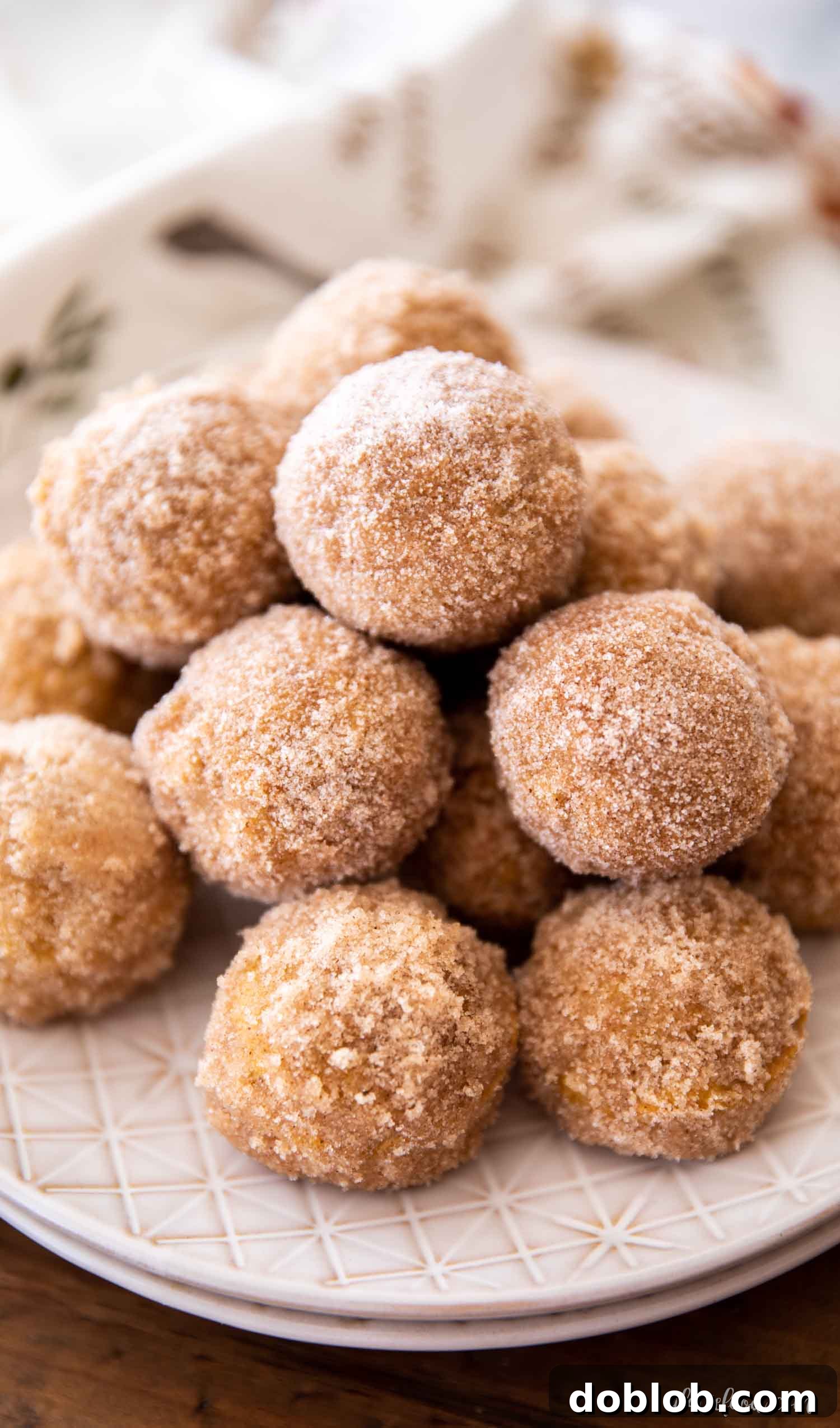 Easy Homemade Baked Pumpkin Donut Holes A rustic shot of baked pumpkin donut holes lavishly coated in cinnamon sugar, arranged on a brown wooden board, highlighting their perfect golden brown texture.