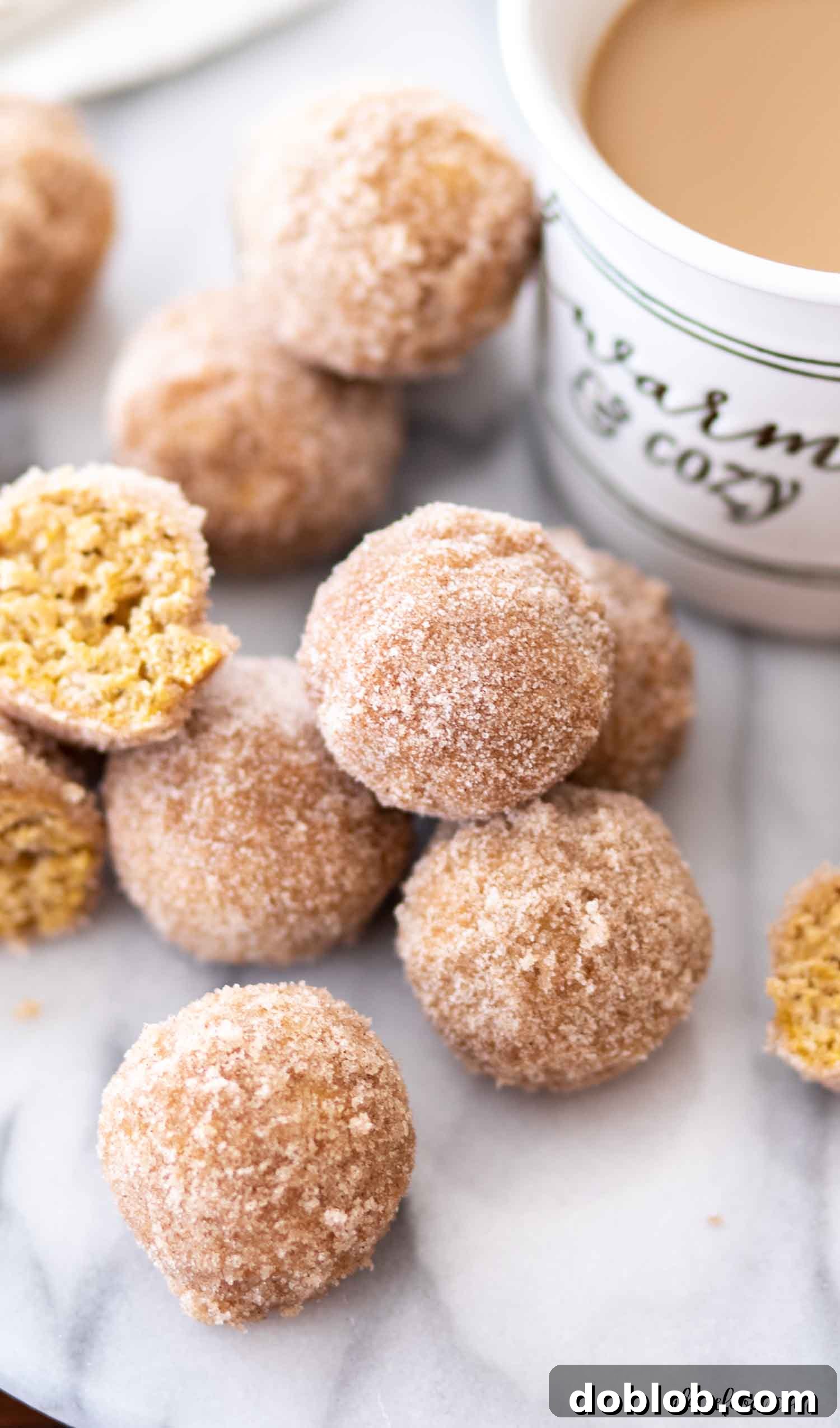 Pumpkin Donut Holes with Coffee for Breakfast A stack of warm, baked cinnamon sugar pumpkin donut holes on a marble board, accompanied by a steaming cup of coffee – the ideal pairing for a cozy fall morning.