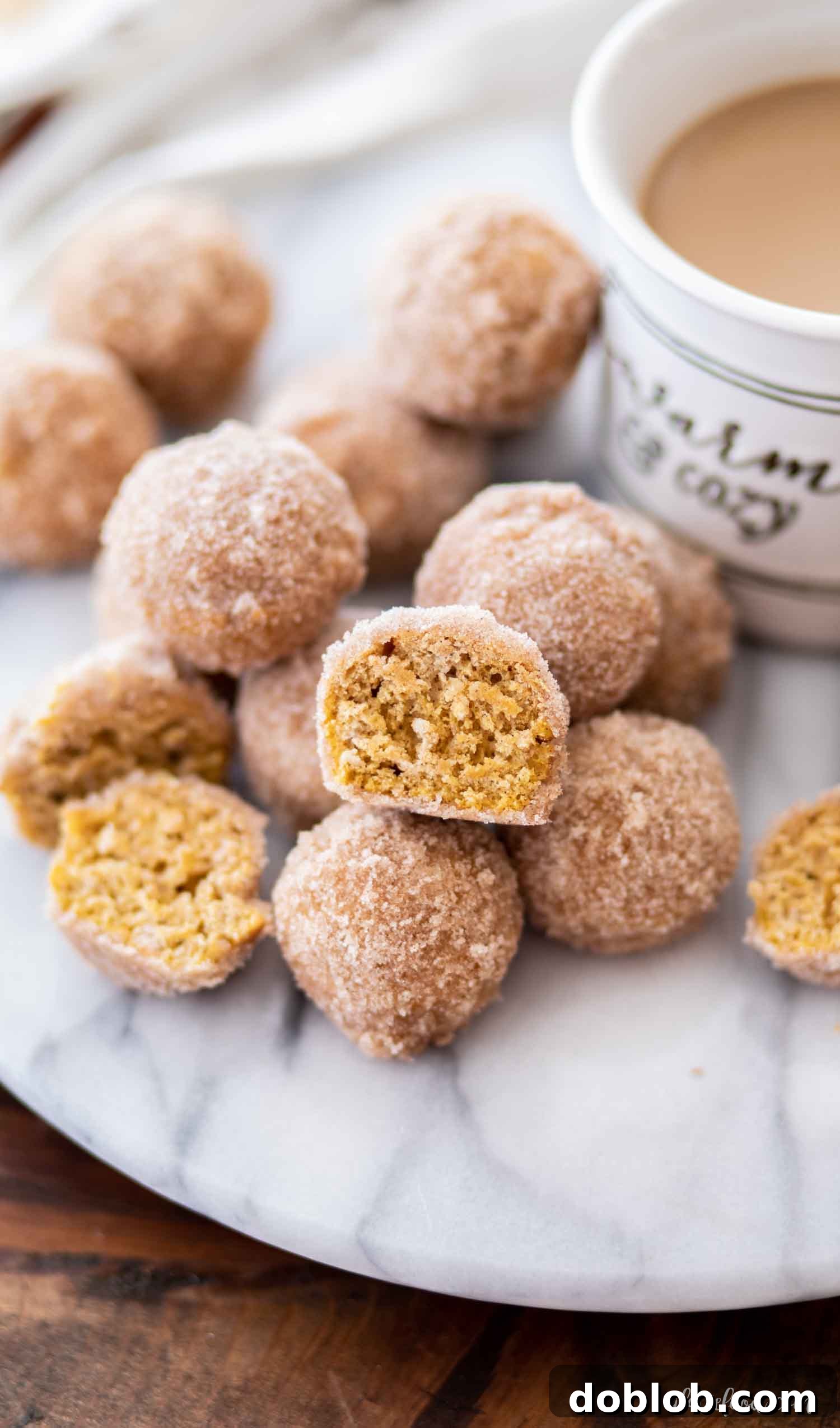 Homemade Baked Pumpkin Donut Holes with Cinnamon Sugar A stack of freshly baked pumpkin donut holes, glistening with cinnamon sugar, next to a cup of coffee on a elegant marble board, perfect for a gourmet breakfast.