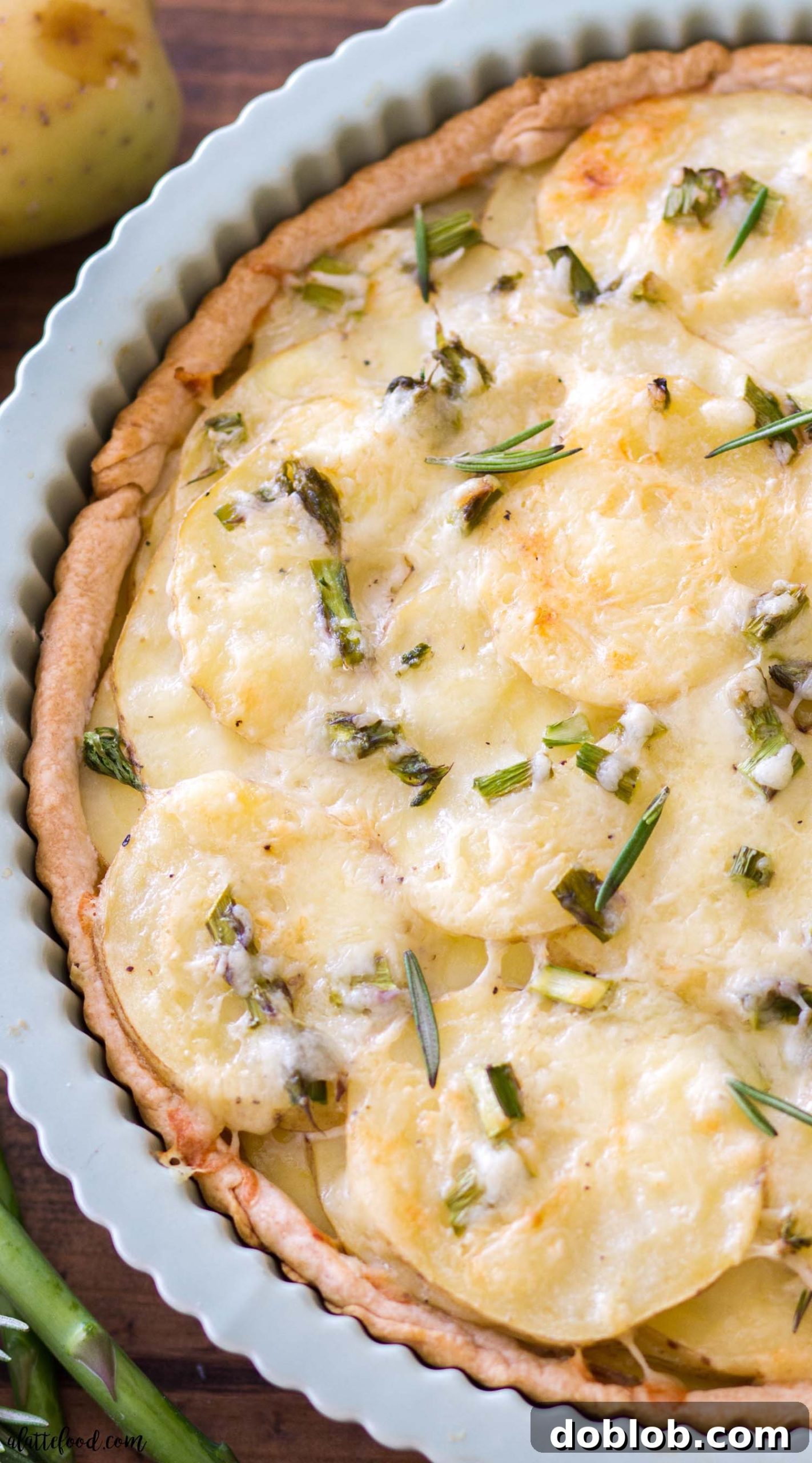 Ingredients for Cheesy Asparagus Potato Tart arranged on a cutting board, including thinly sliced potatoes, asparagus, cheese, and fresh rosemary.