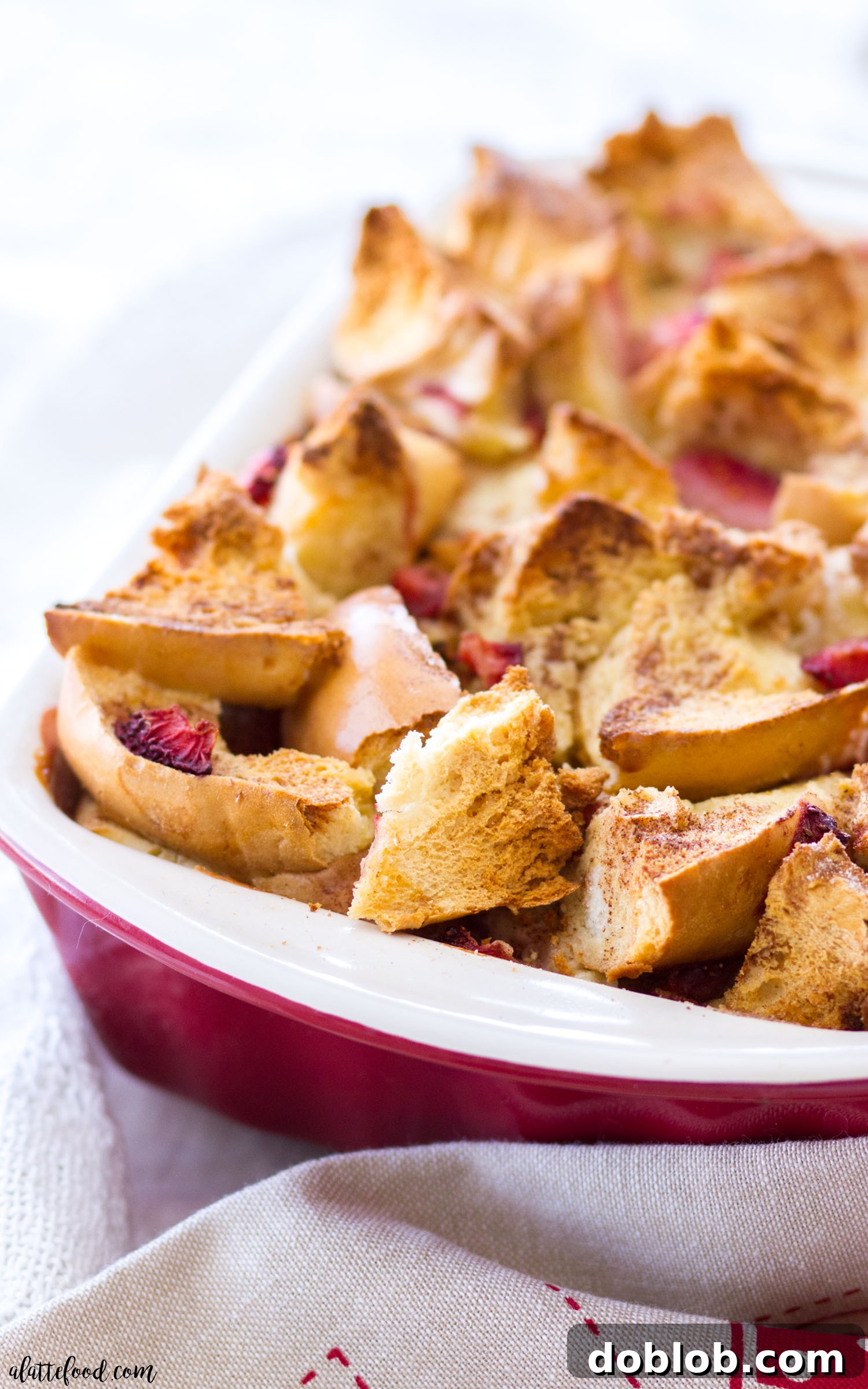 A close-up shot of the Bagel and Cream Cheese Strawberry French Toast Casserole, featuring plump strawberries and melted cream cheese on top of golden bagels.