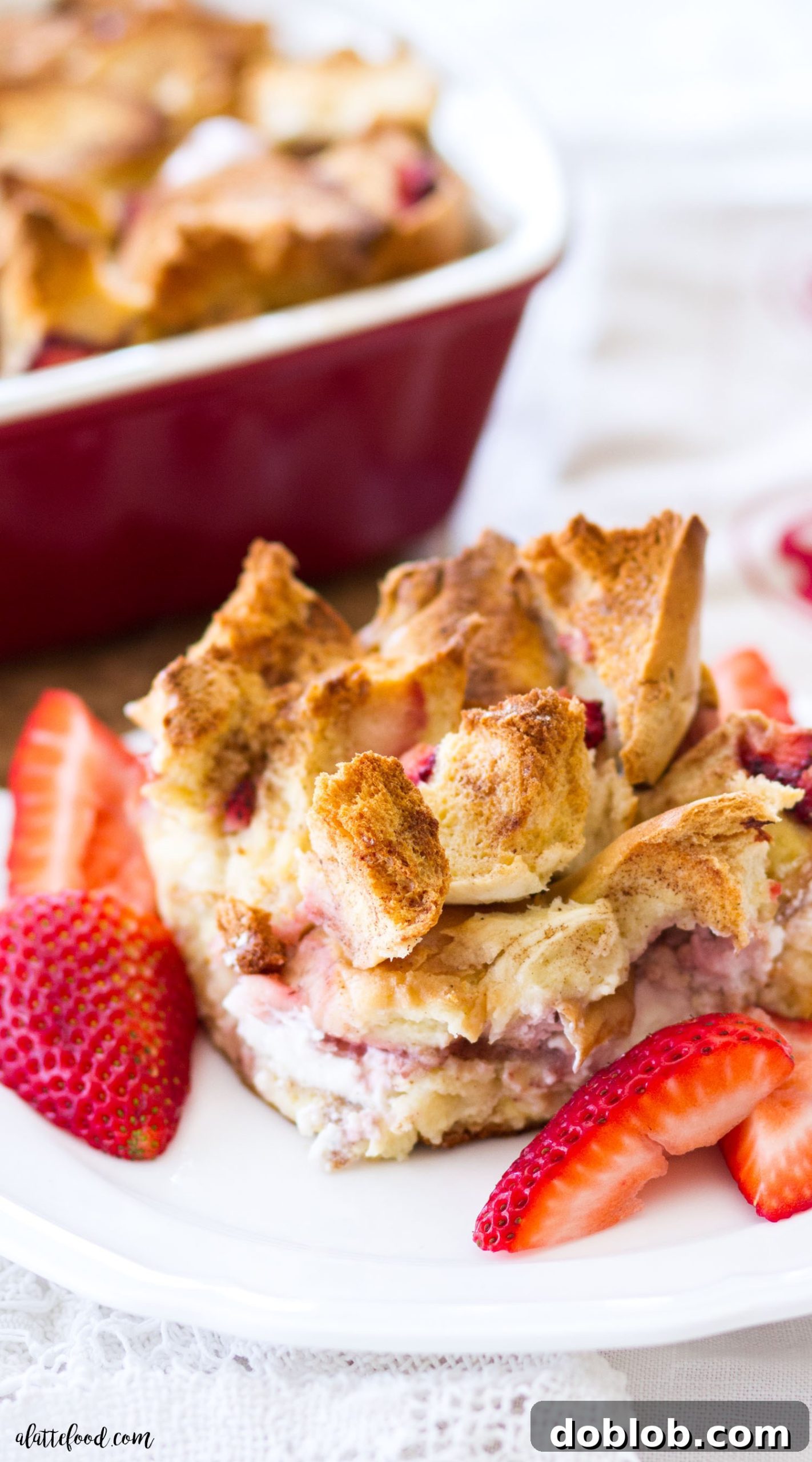 A close-up of a serving of Bagel and Cream Cheese Strawberry French Toast Casserole, showcasing the fluffy texture and colorful fruit against a rustic wooden background.