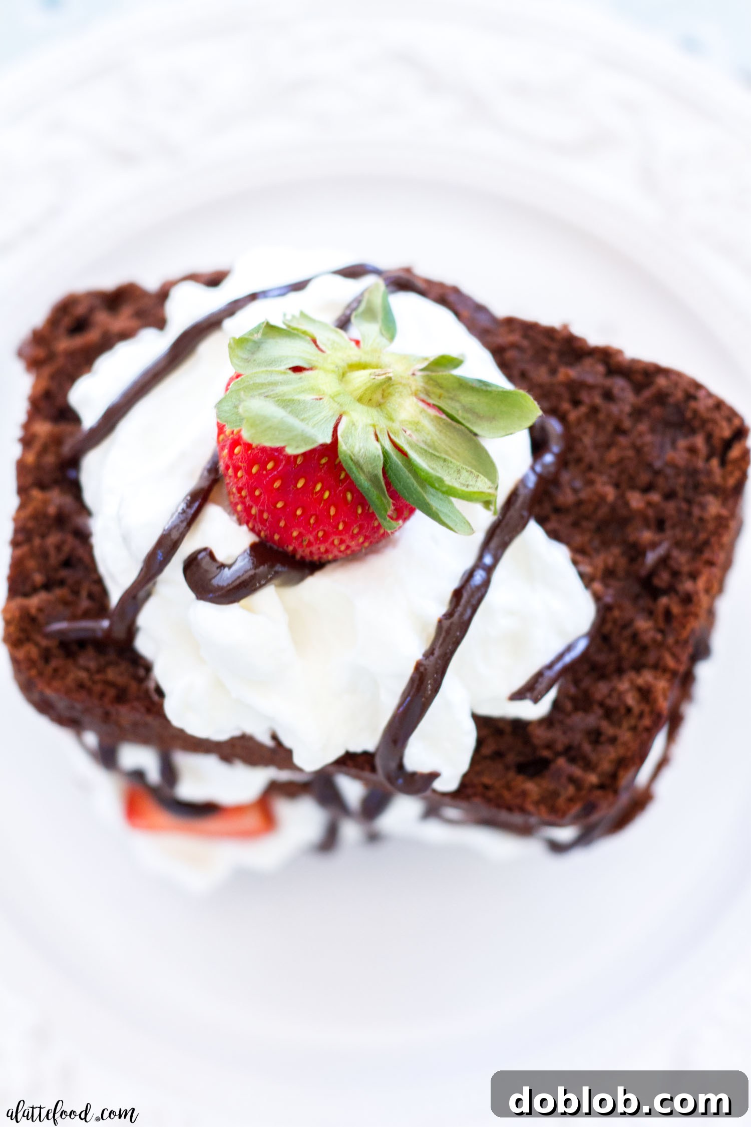 A close-up of a slice of Chocolate Espresso Pound Cake drizzled with ganache and topped with whipped cream and strawberries
