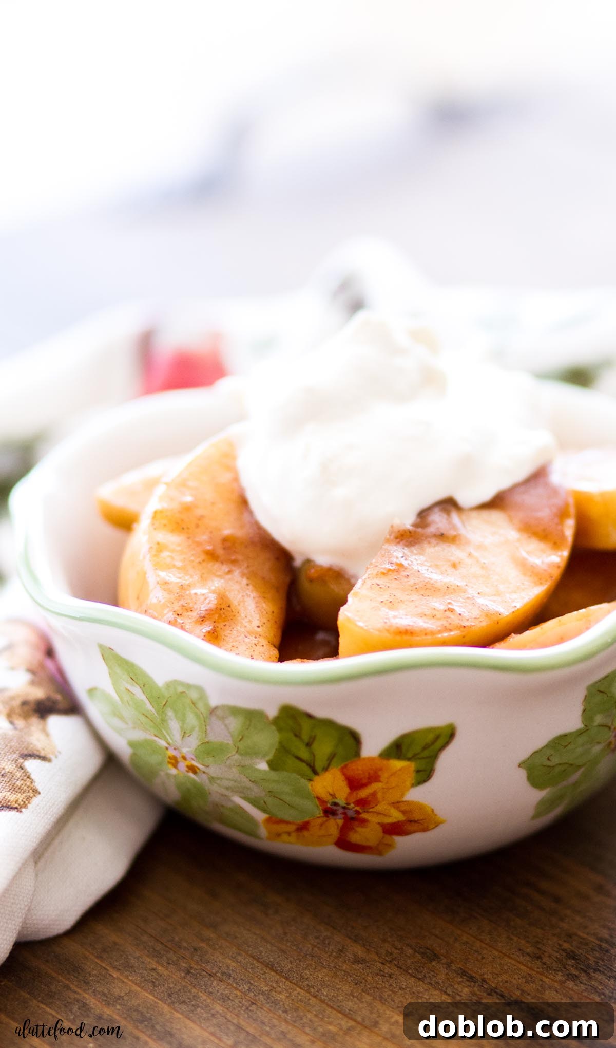 Cinnamon spiced apples in a flowered bowl topped with whipped cream, perfect for Thanksgiving or Christmas.